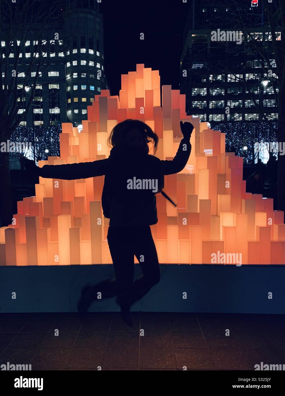 Girl jumping in front of orange pyramid light installation Canary Wharf - Smartphone Captured Stock Image