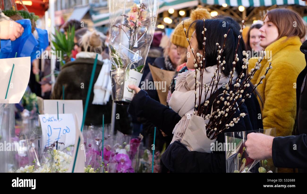 Flower stall, lady buying an orchid in a busy market. - Smartphone Captured Stock Image