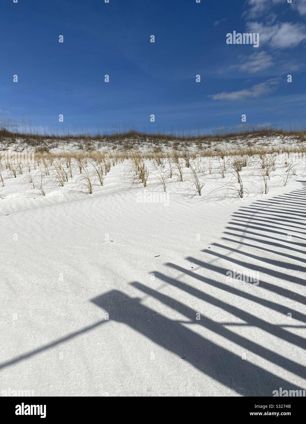 White sand beach with shadows of wooden fence cast upon the sand Stock Photo