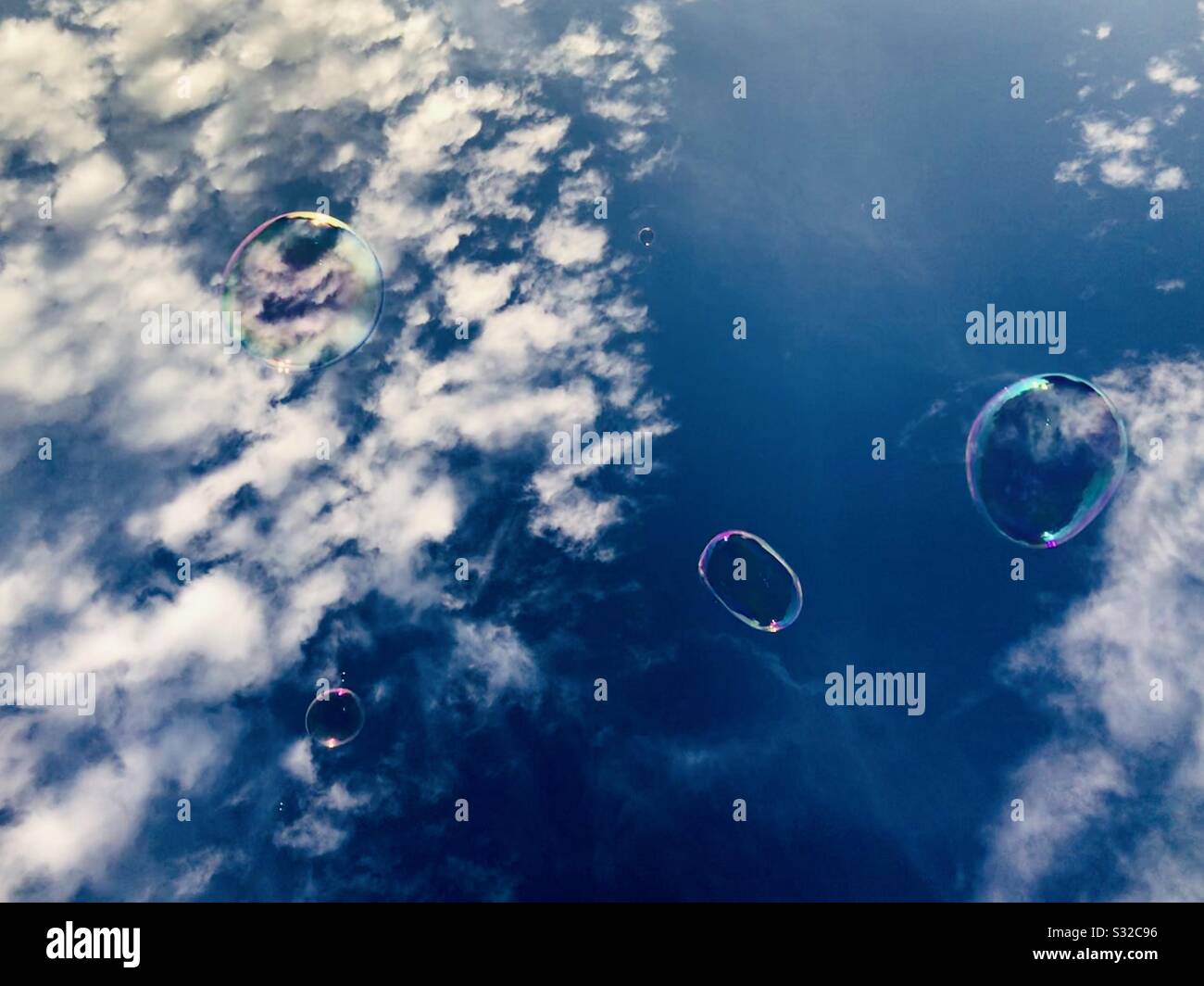 Soap bubbles floating away against a deep blue summertime sky. Stock Photo