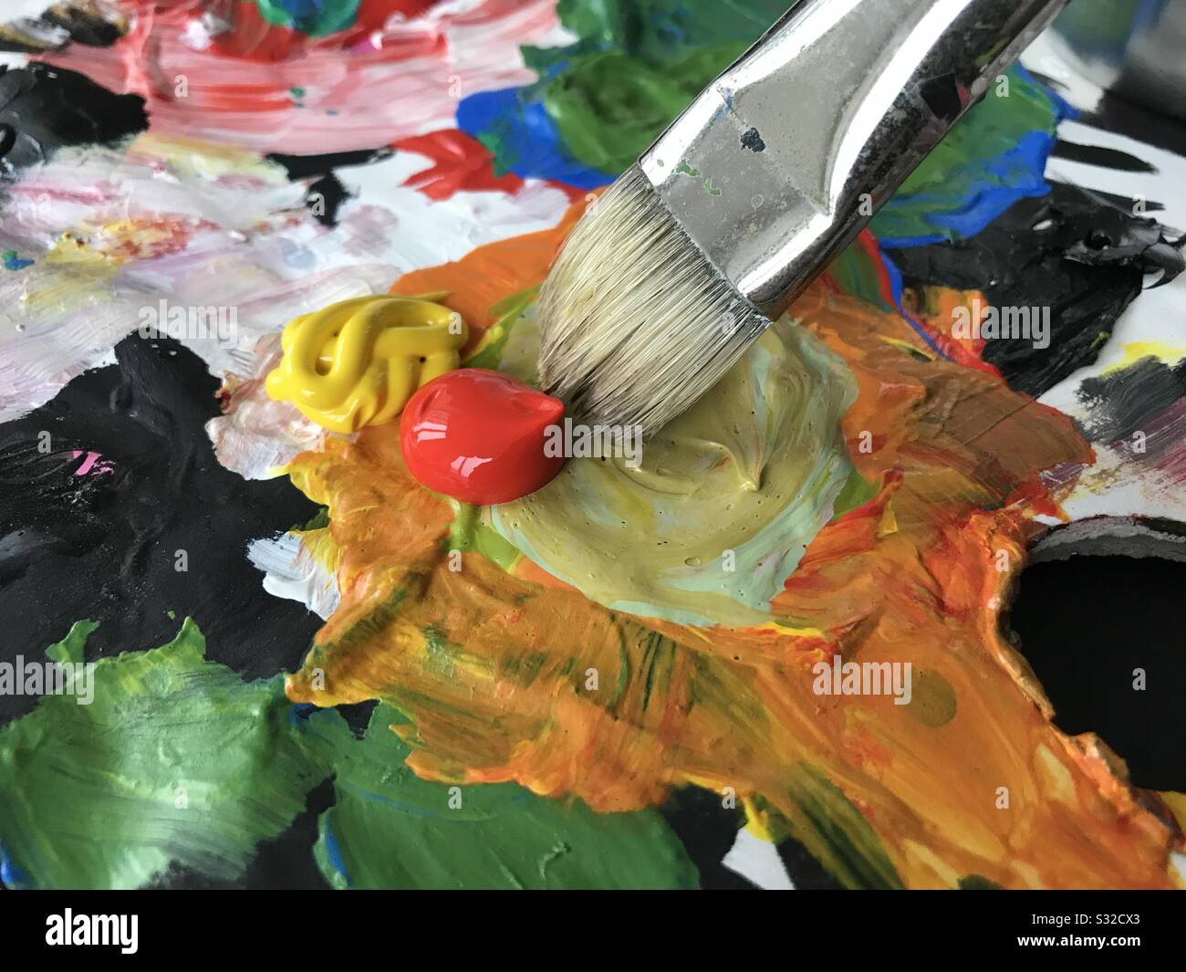 Painters palette with brush mixing red and yellow paint. Stock Photo
