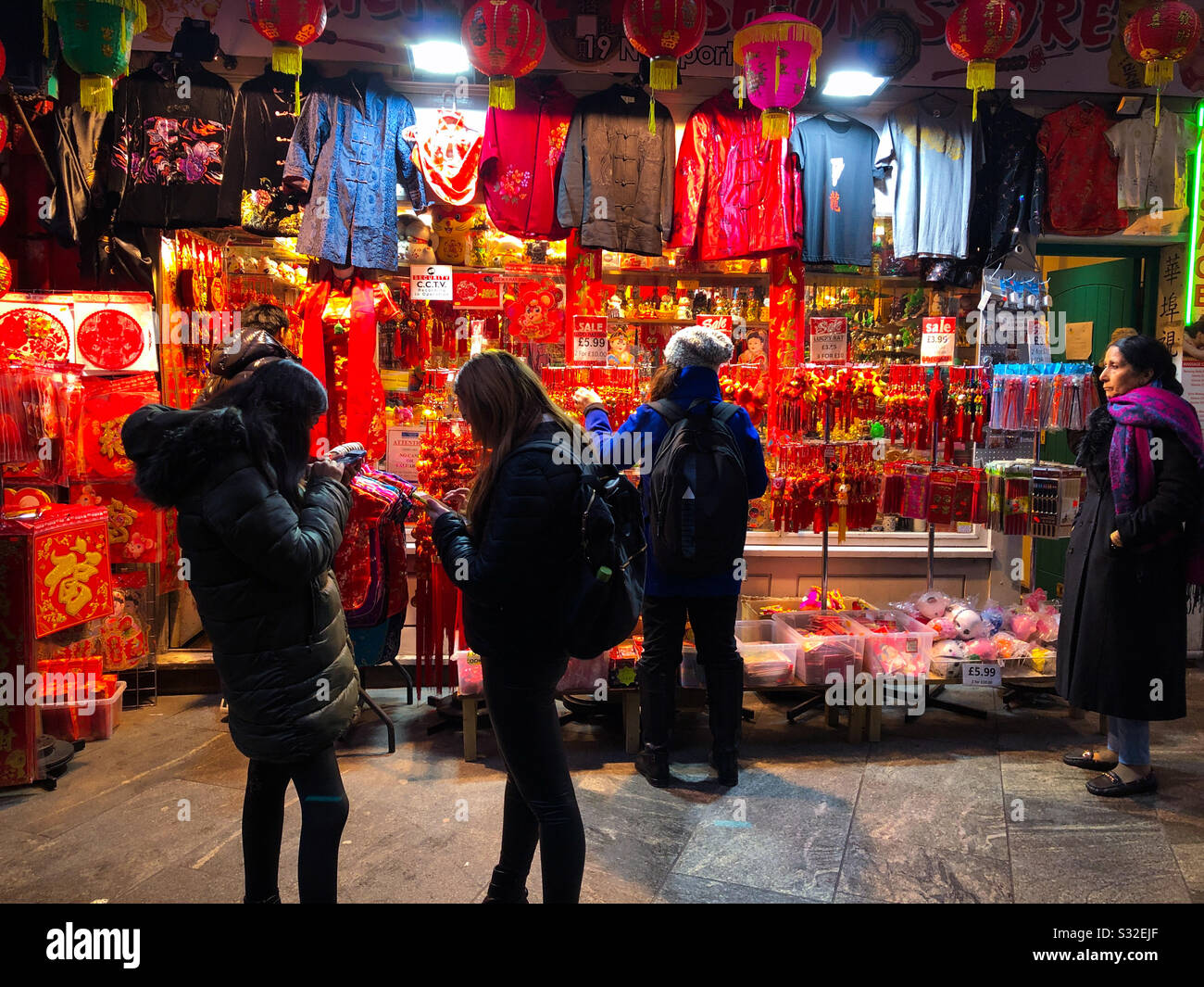 People including Chinese girls on mobile phones, outside a shop selling clothes and accessories decorated for Chinese New Year, Chinatown, London, England Stock Photo