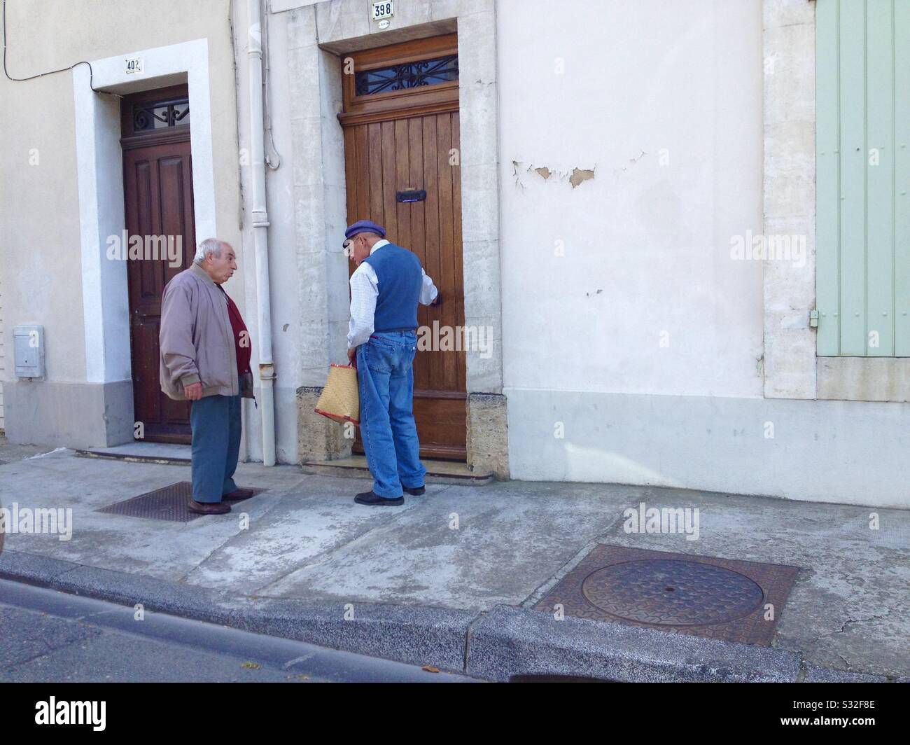 Two Frenchmen converse on a street in the town of Cavaillon, Côte d’Azur, Provence, France. - Smartphone Captured Stock Image