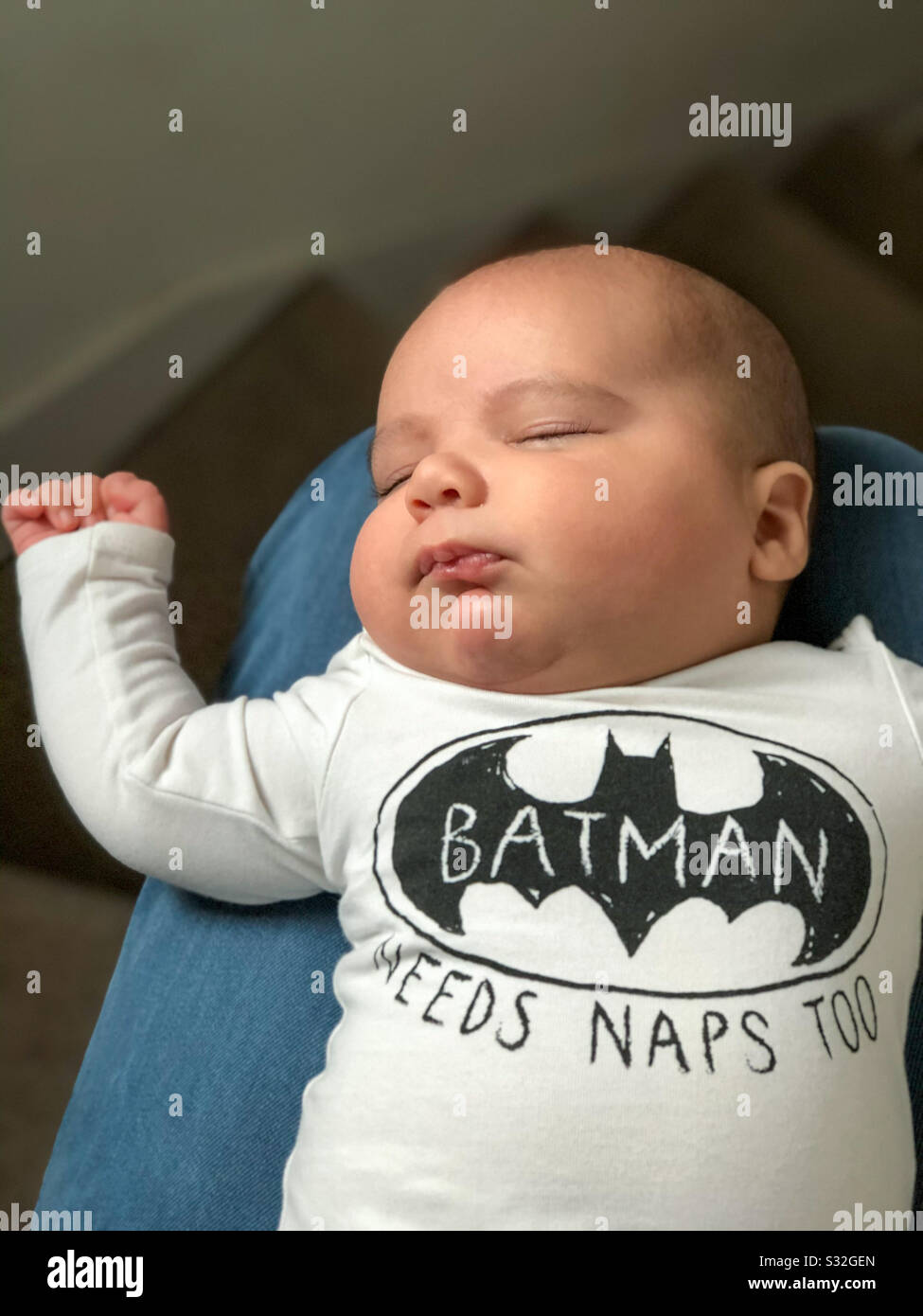 An 8 week old baby boy napping on his fathers lap whilst dressed as Batman. - Smartphone Captured Stock Image