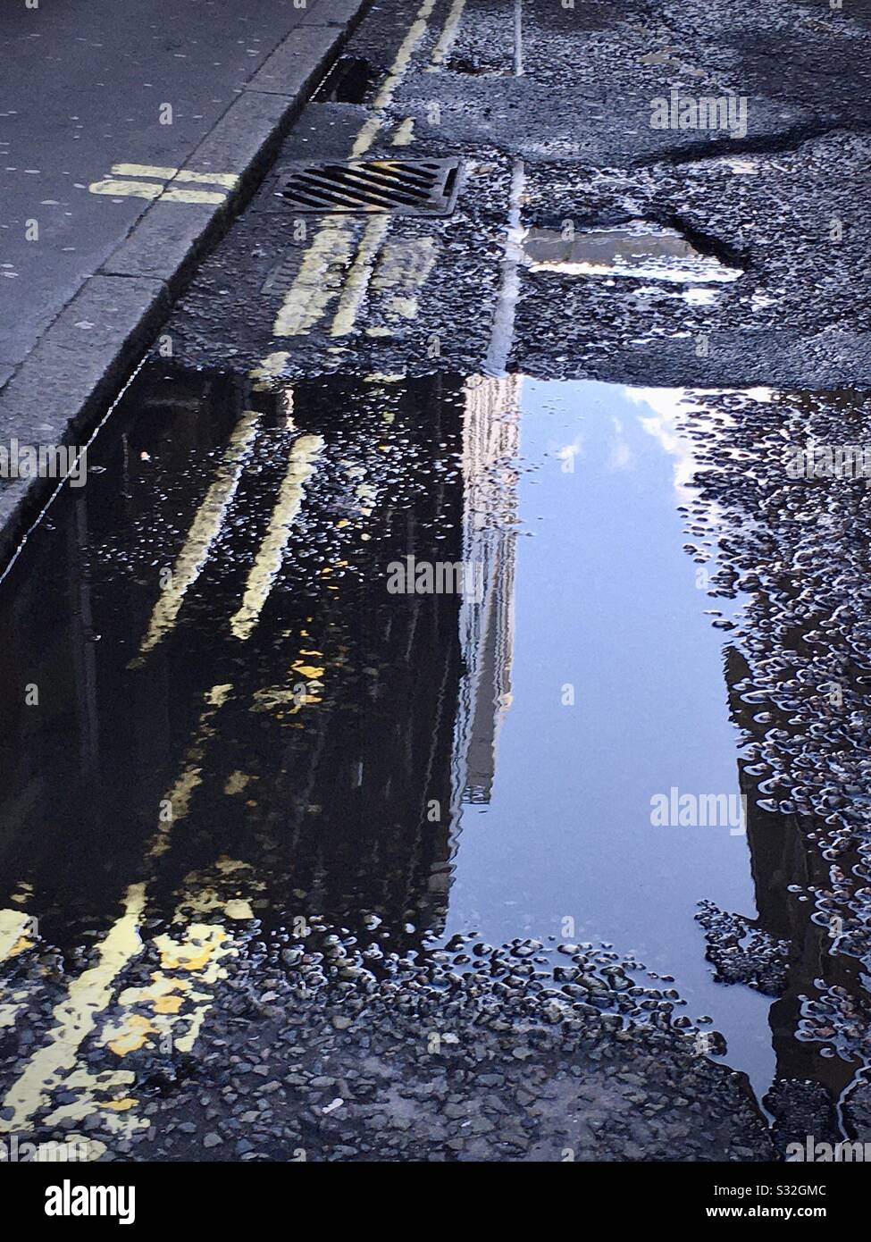 Road with yellow parking lines and pavement with a reflection in a puddle, - Smartphone Captured Stock Image