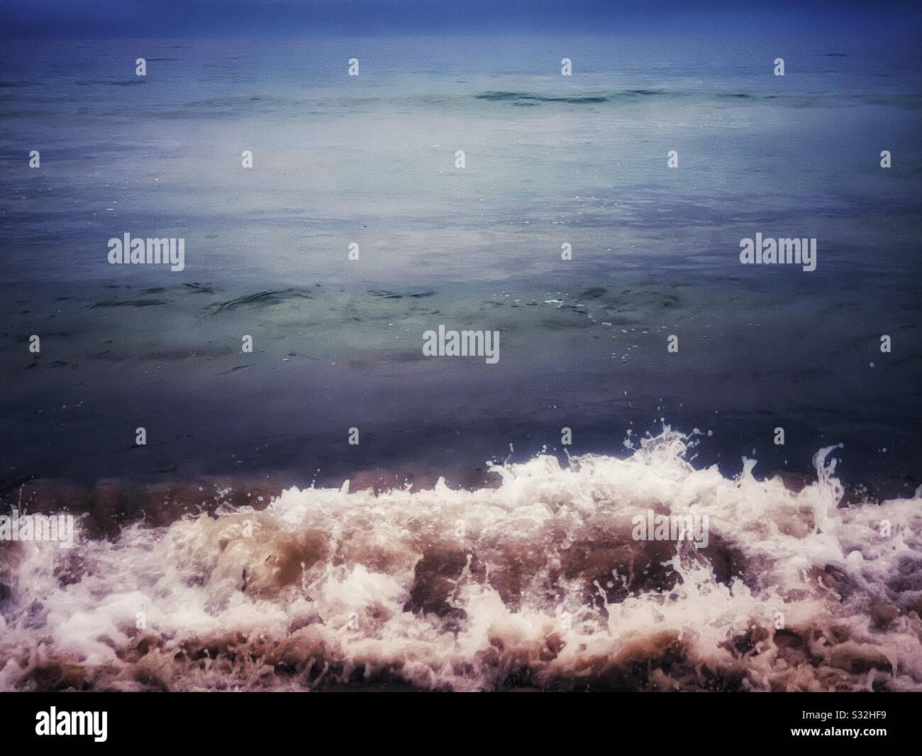 Splashing and crashing, sandy, frothy sea waves meet shore at the beach - Smartphone Captured Stock Image