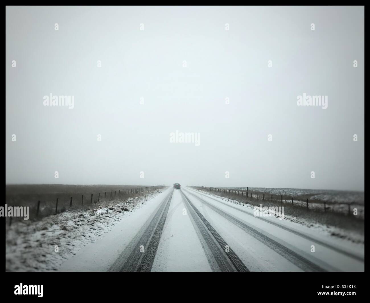 One distant car driving in the snow on a road across the moors in winter Stock Photo