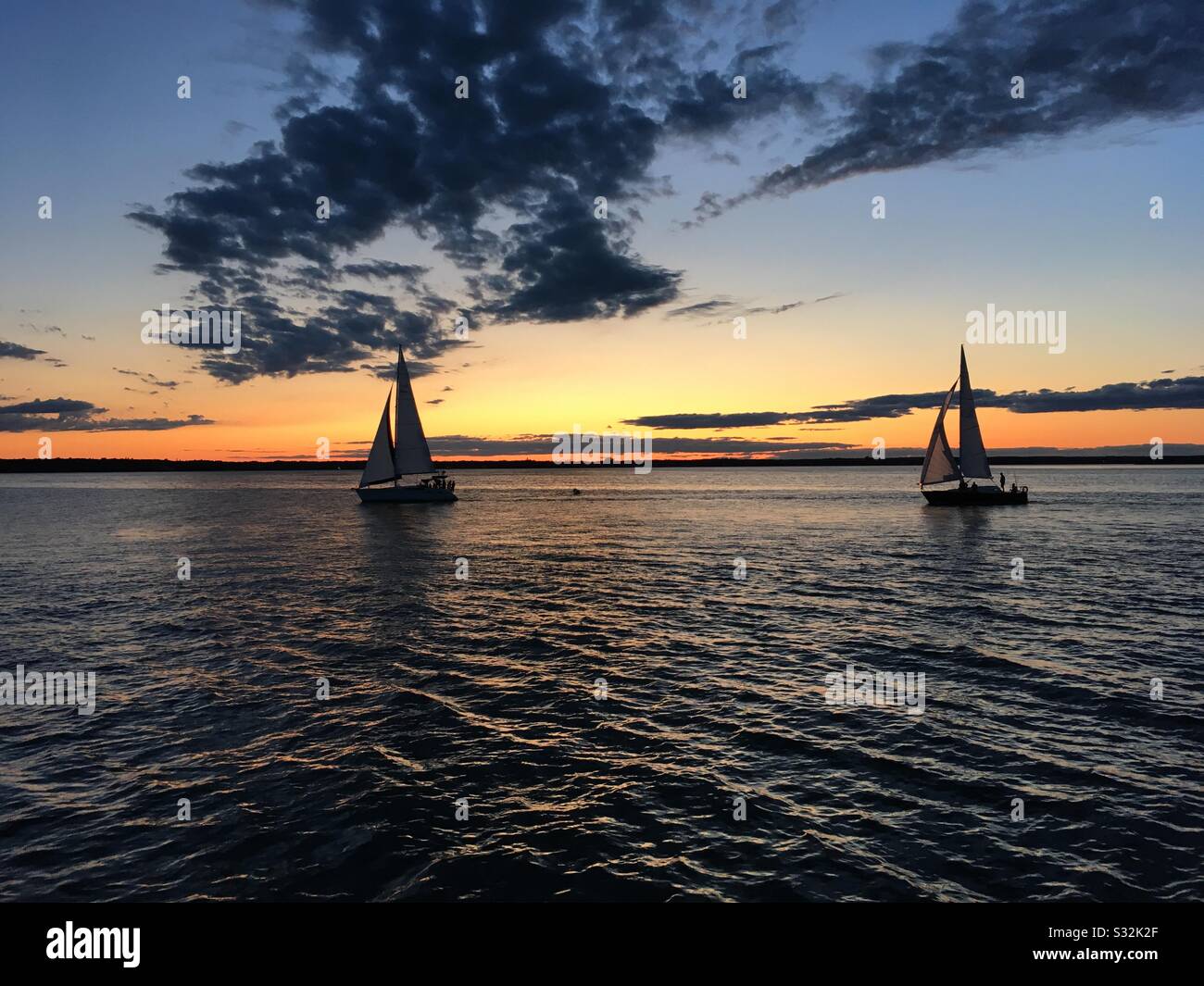 Sailboats sailing on calm ocean waters in maritime harbour at sunset