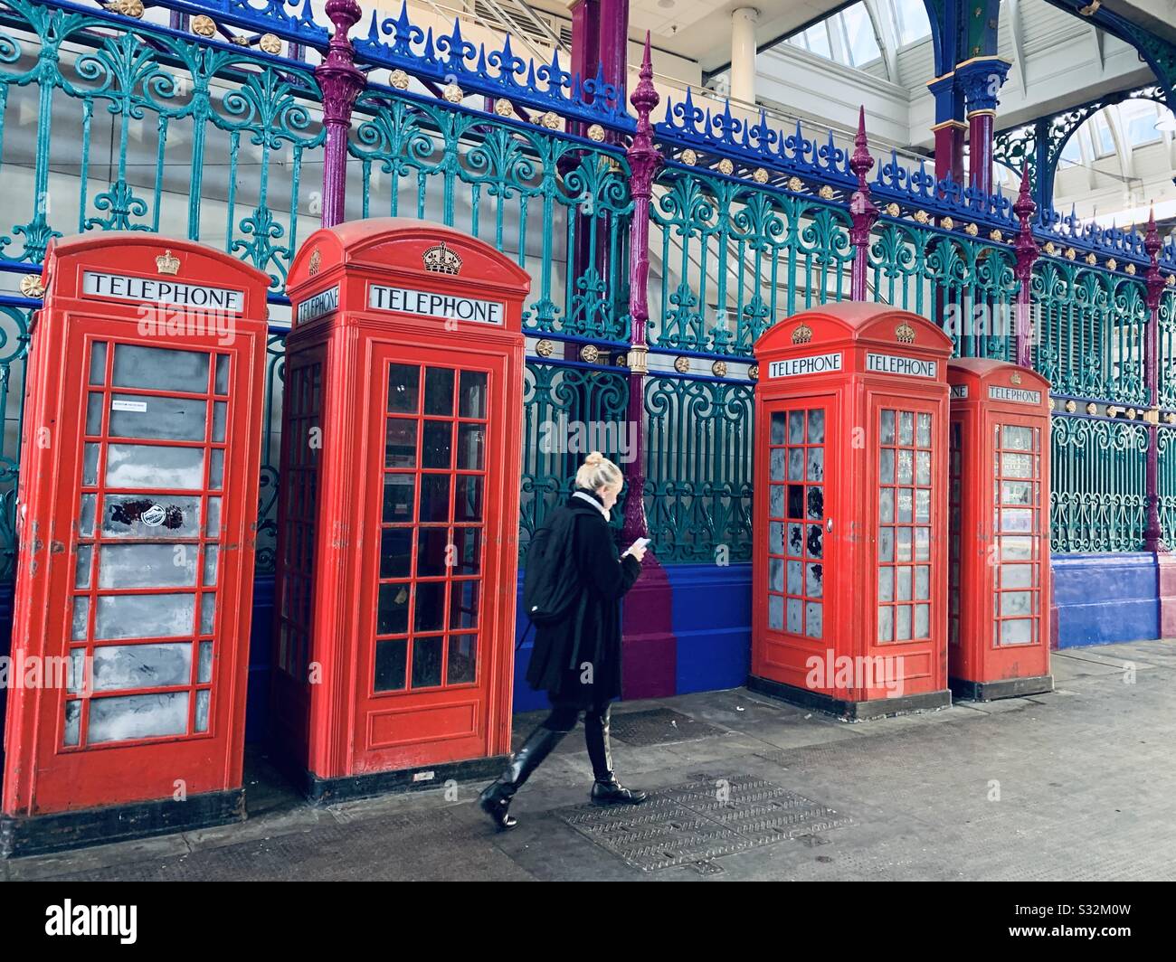 Female commuter walking past red phone boxes against colourful gate in Farringdon Stock Photo