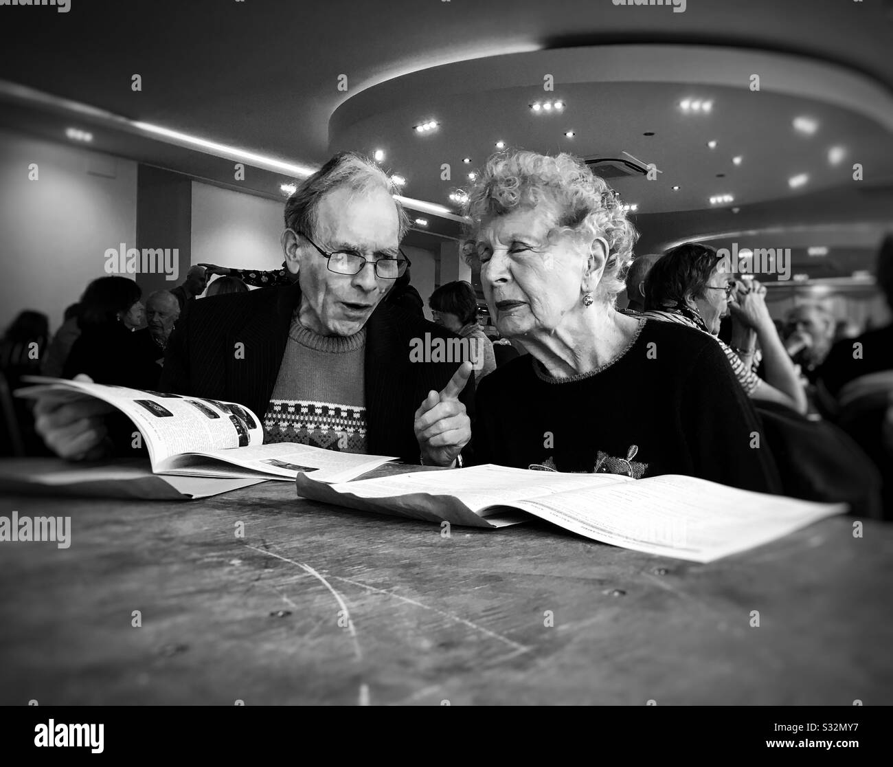 Two senior citizens in lively discussion at  a U3A meeting; six other people in the background. - Smartphone Captured Stock Image