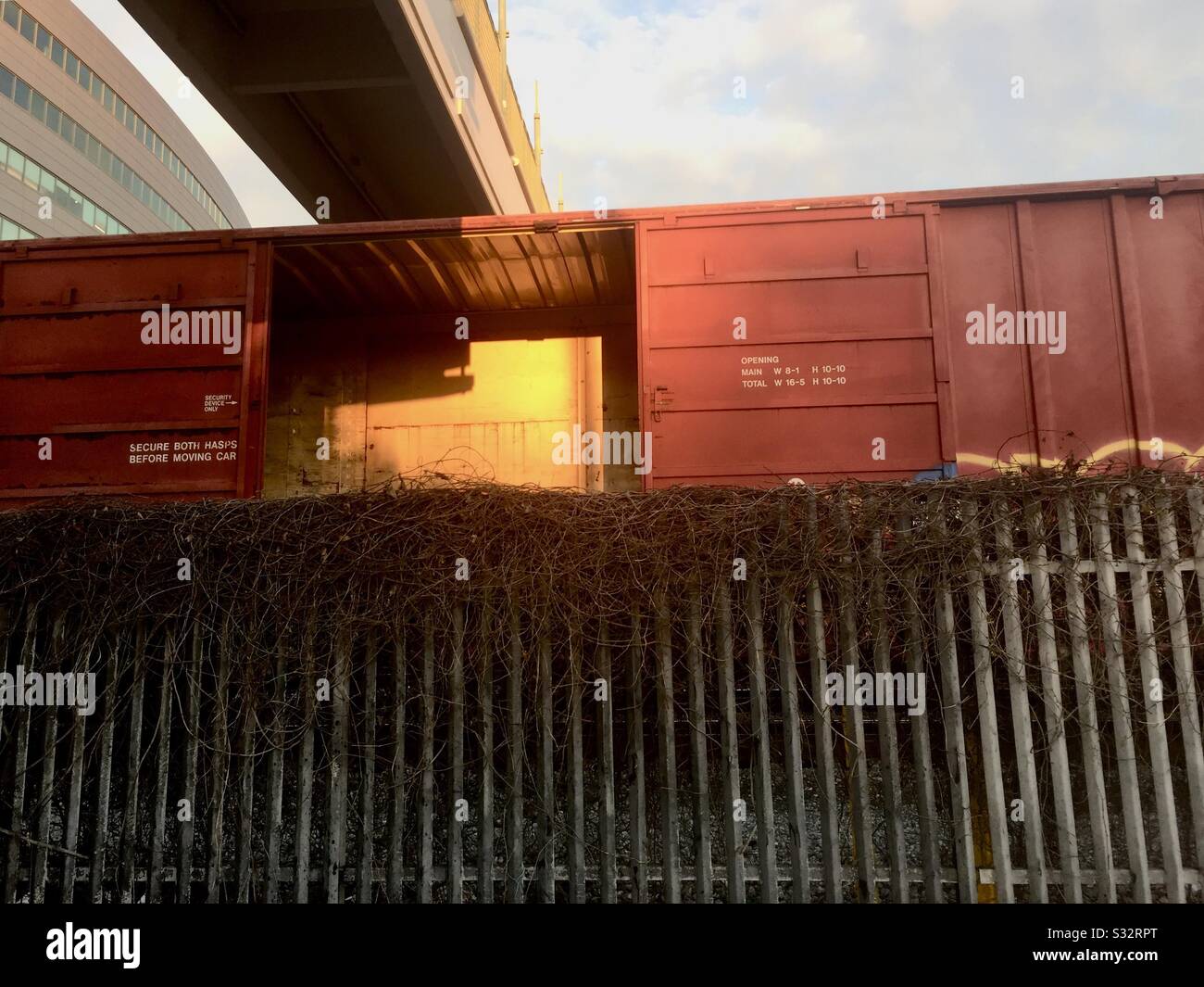 Empty boxcar of a freight train behind a fence under a cement bridge reflecting the sun in Emeryville, California. - Smartphone Captured Stock Image