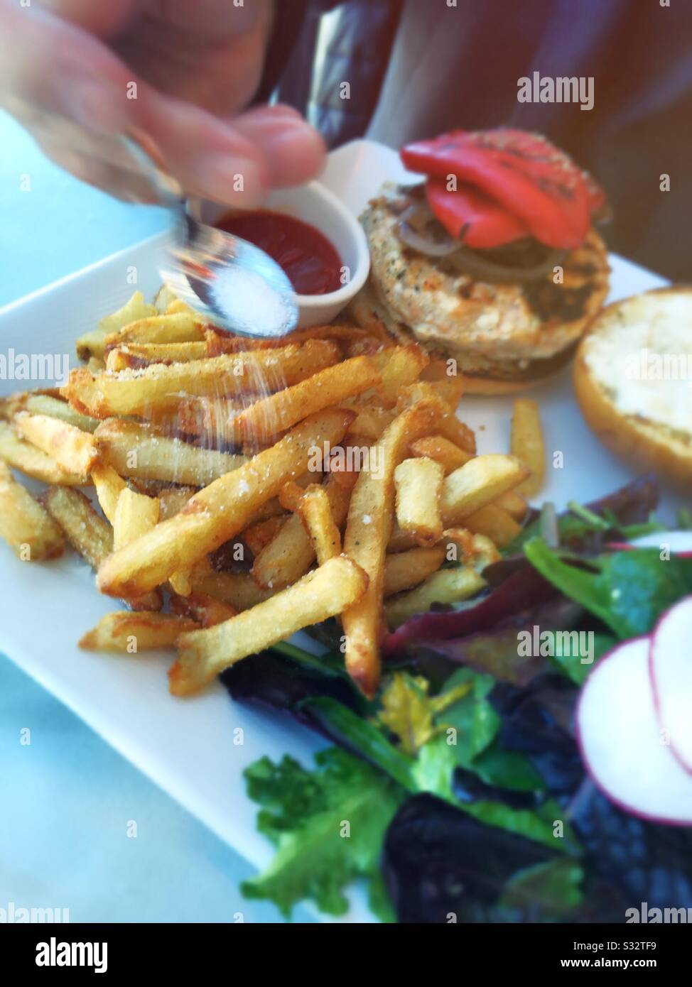 Male diner salting his french fries as part of a gourmet lunch with a salmon burger, USA - Smartphone Captured Stock Image