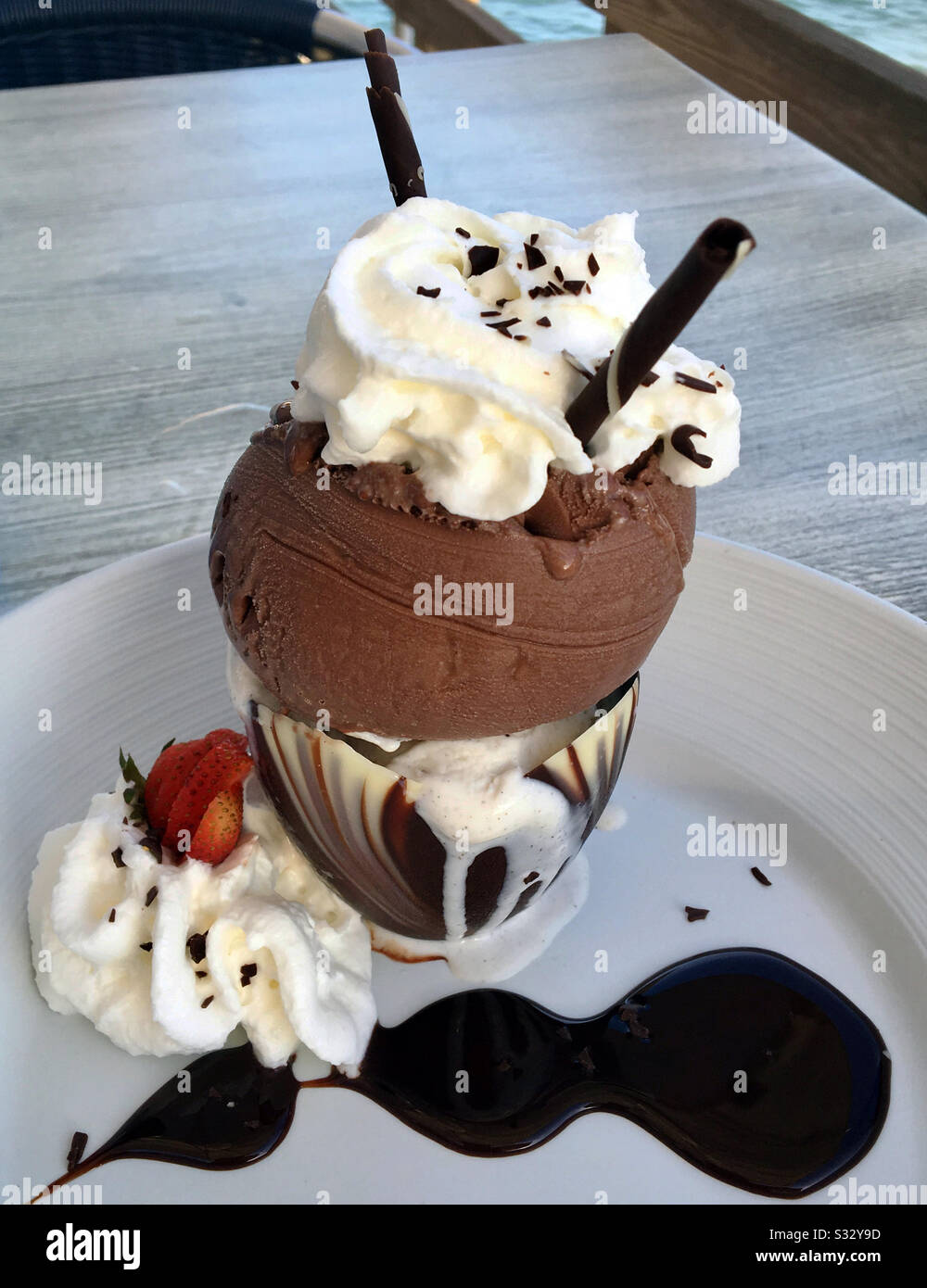 Decadent dessert dish of chocolate ice cream with whipped cream, chocolate straws, a strawberry and chocolate sauce garnishes. - Smartphone Captured Stock Image