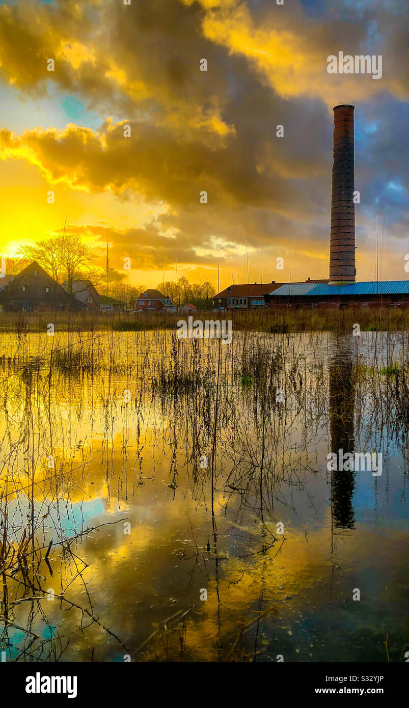 Dramatic and colorful sunset and ruins of an old stone factory reflected in the water of a puddle in the grass - Smartphone Captured Stock Image