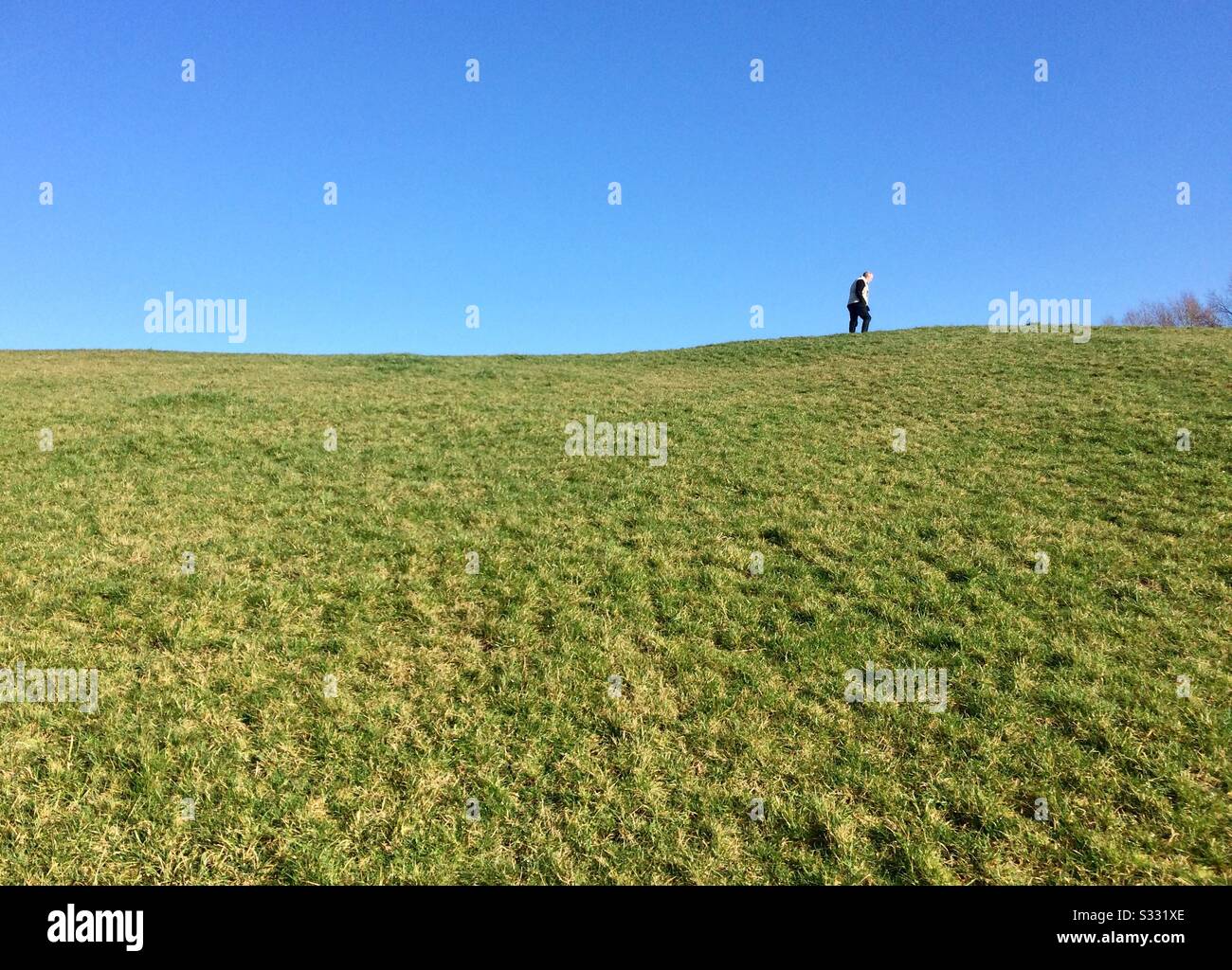 Lone Man on the horizon, walking along the ridge of a hill against a bright blue sky. England UK - Smartphone Captured Stock Image