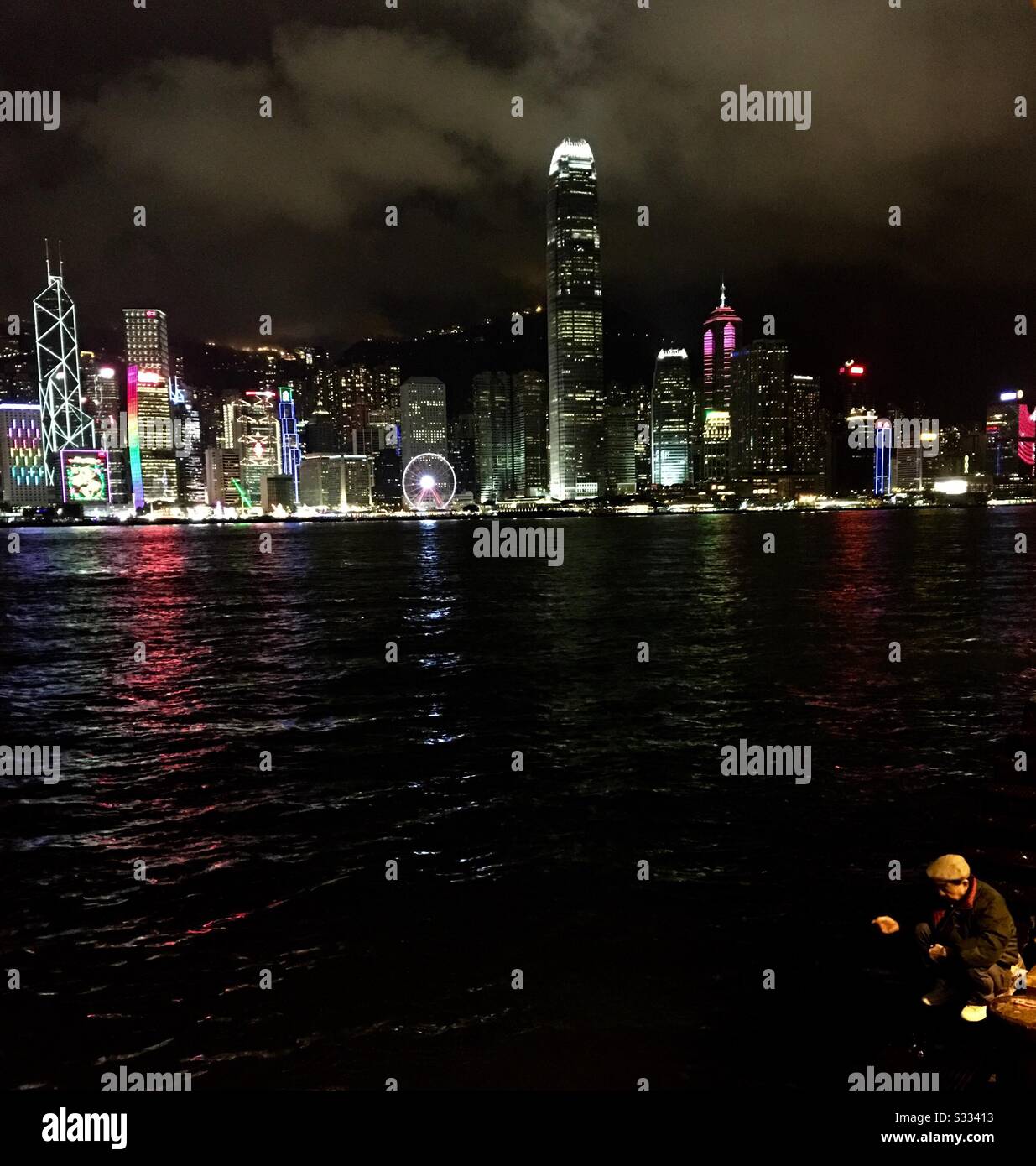 A Chinese fisherman fishing in Victoria harbour with the beautiful skyline of Hong Kong behind him. - Smartphone Captured Stock Image