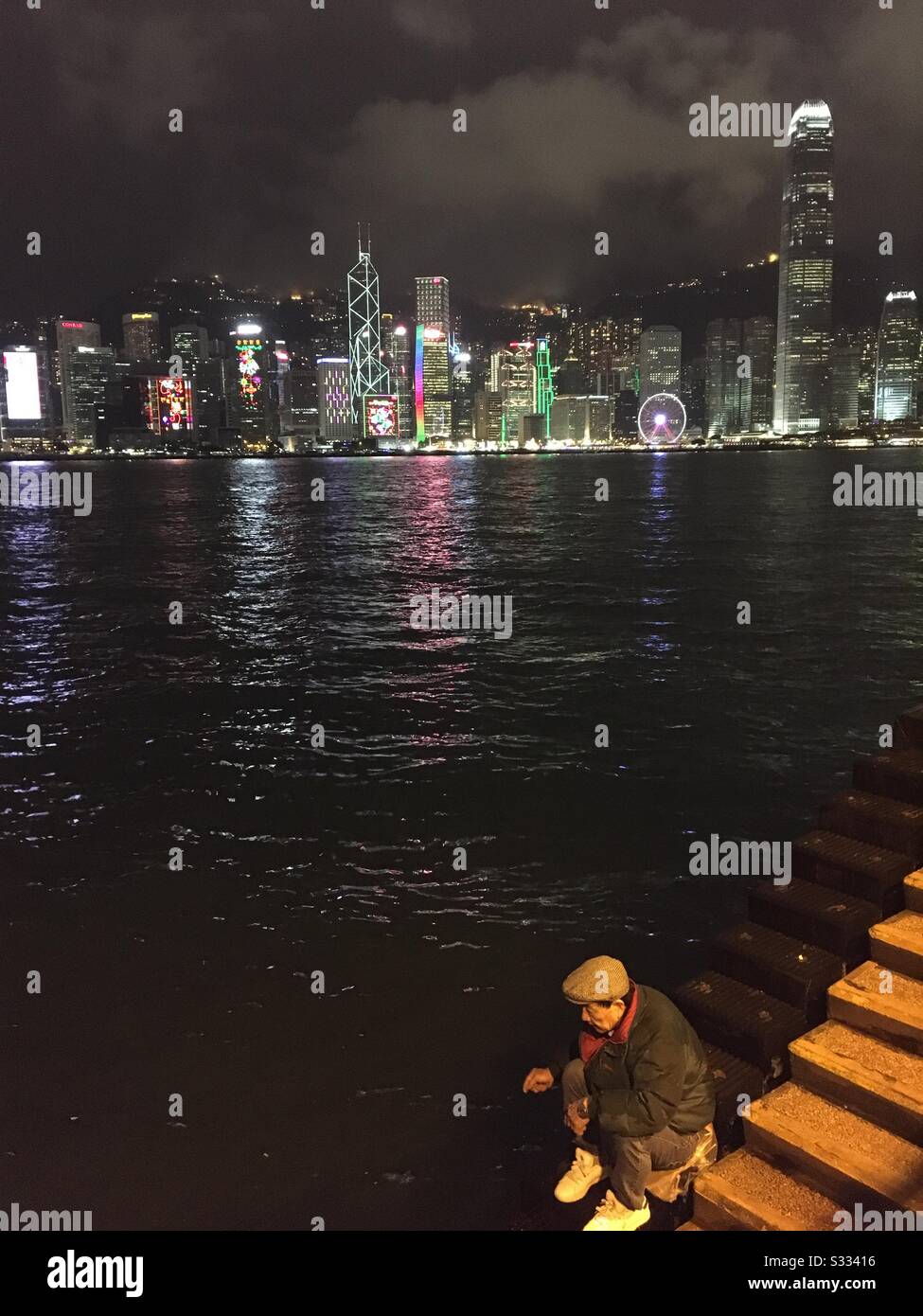 A Chinese fisherman fishing in Victoria harbour with the beautiful skyline of Hong Kong behind him. - Smartphone Captured Stock Image