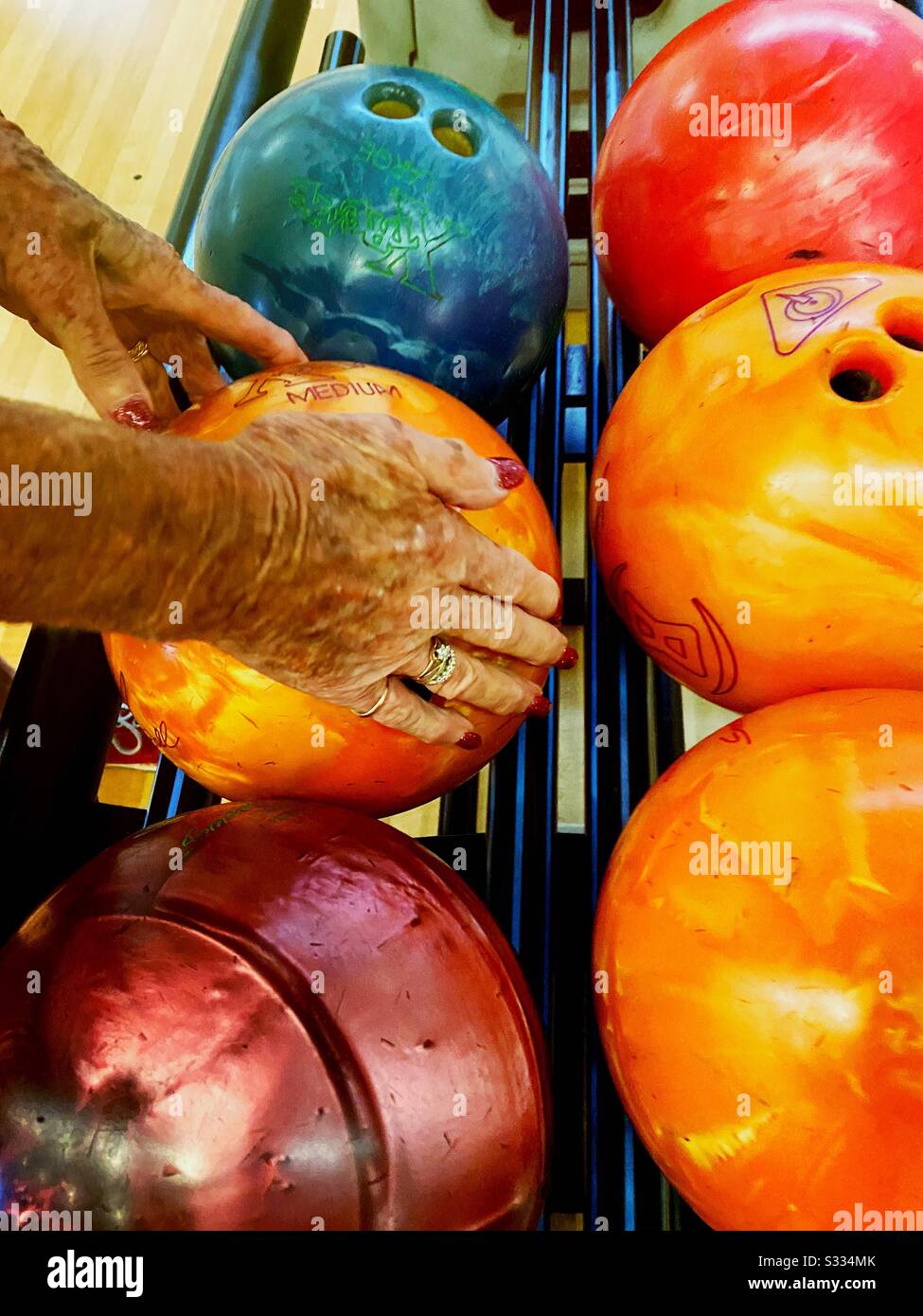 Hands of senior female collecting ten pin bowling ball. Active lifestyle and indoor recreational sports for mature people Stock Photo