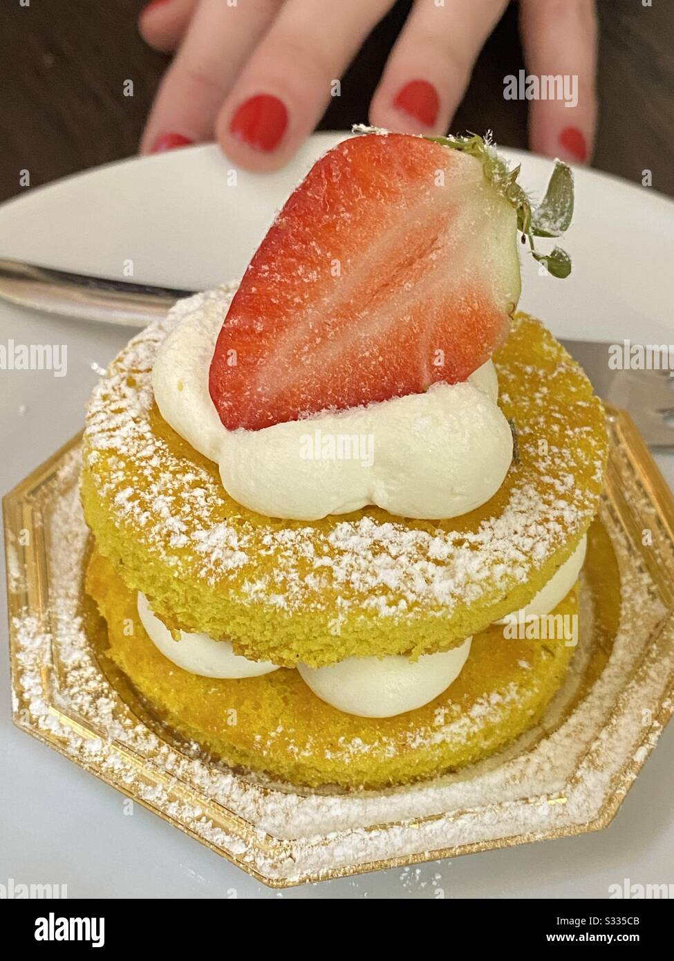 Luxury pastry with cream, strawberry and a woman hand with red nails painted red - Smartphone Captured Stock Image