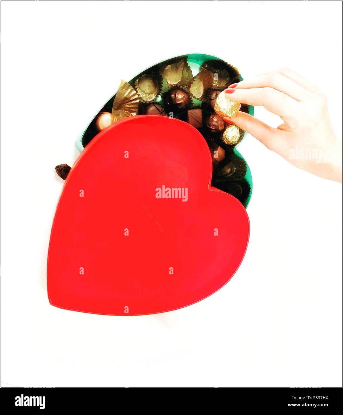 Heart shaped box of chocolates with a female hand holding a chocolate. - Smartphone Captured Stock Image