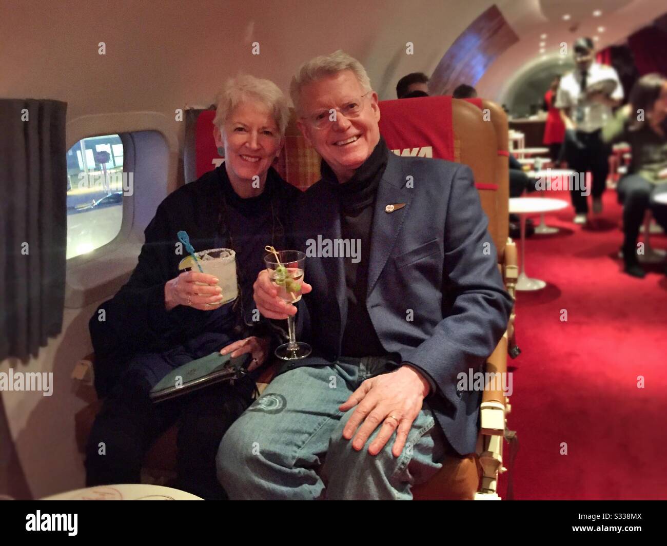 Upscale successful couple enjoying cocktails at the Connie, a cocktail lounge in the interior of a 1950s constellation aircraft at the TWA hotel located in JFK Airport, NYC, USA - Smartphone Captured Stock Image
