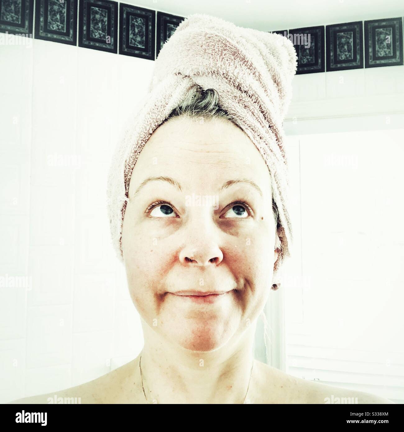 Middle aged woman with towel wrapped on head looking up - Smartphone Captured Stock Image