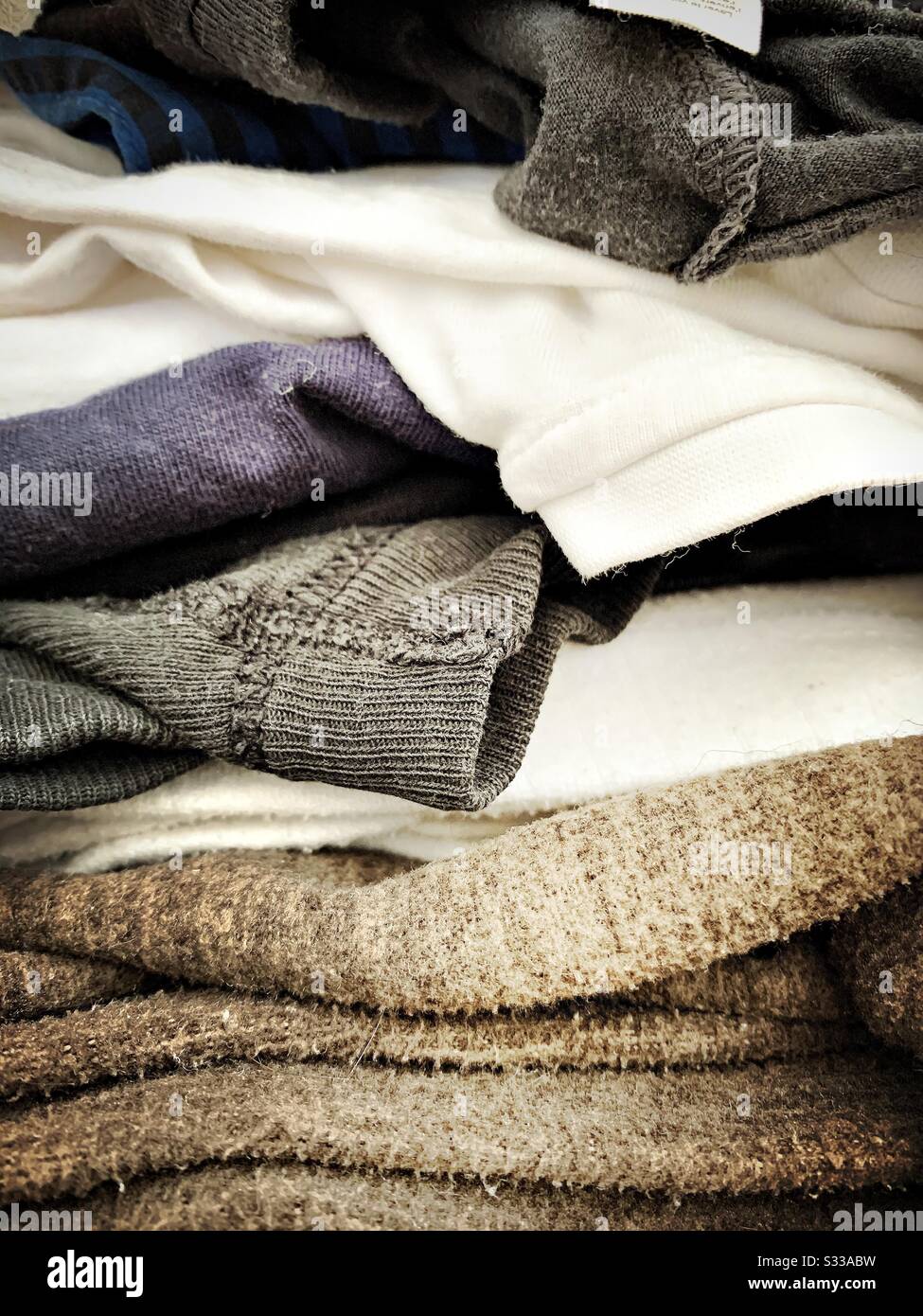 A close up shot on a pile of ironing. Side view of clothes, t shirts, jumpers stacked ready for laundry chores. Detailed view of men’s clothes items. Stock Photo