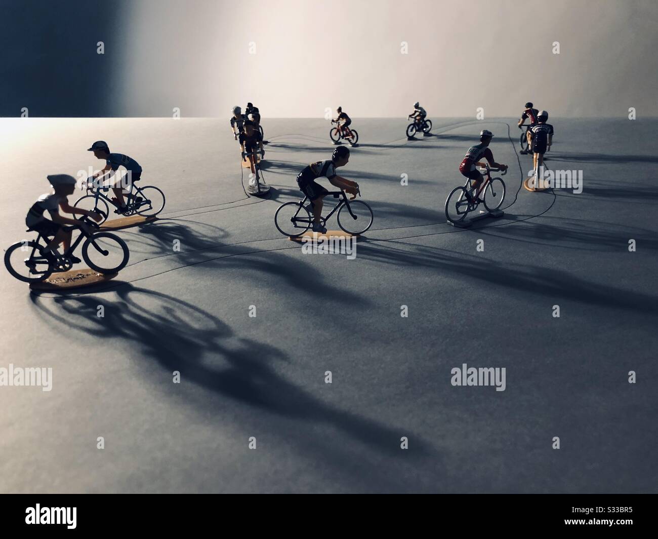 Miniature cyclists with long shadows on grey Stock Photo