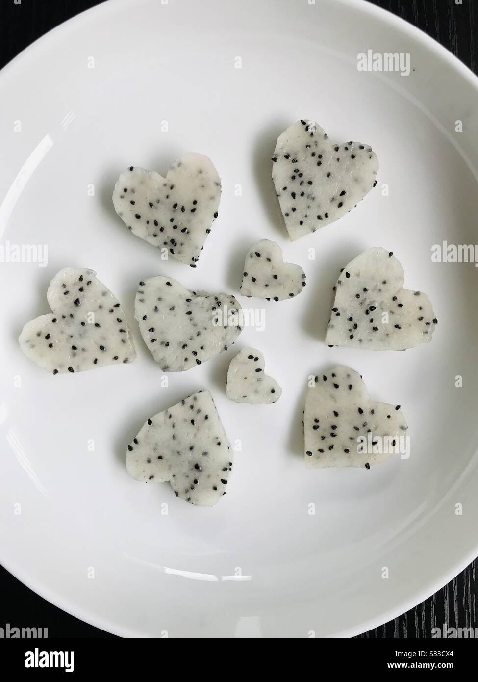 White coloured Dragon fruit - fruit art decoration ,carved in to heart shape in white ceramic plate- colour change mode - kids like to eat shape fruits-fruit hearts Stock Photo