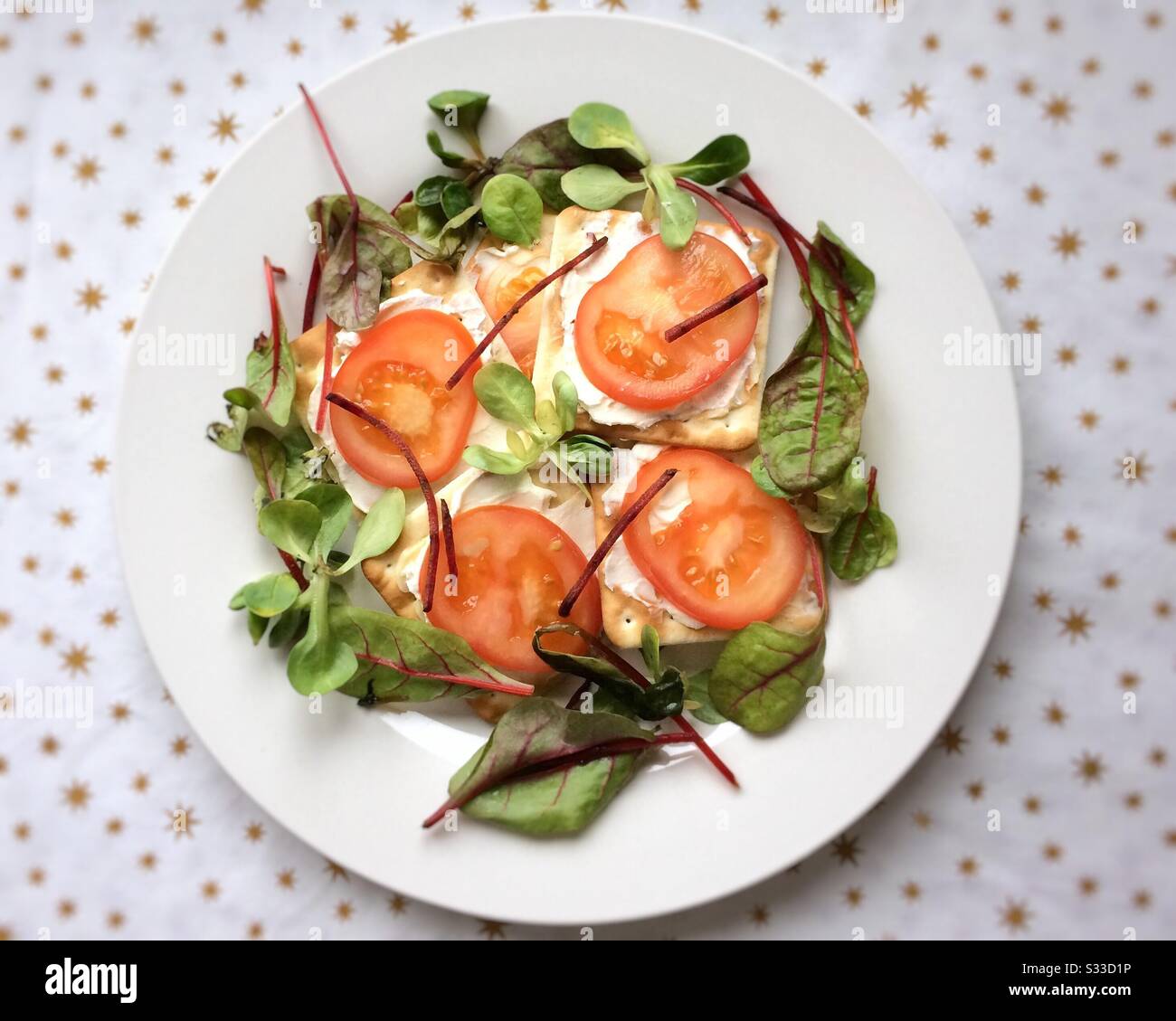 Soft cream cheese, tomatoes on cream crackers, with bistro salad on a white plate. - Smartphone Captured Stock Image