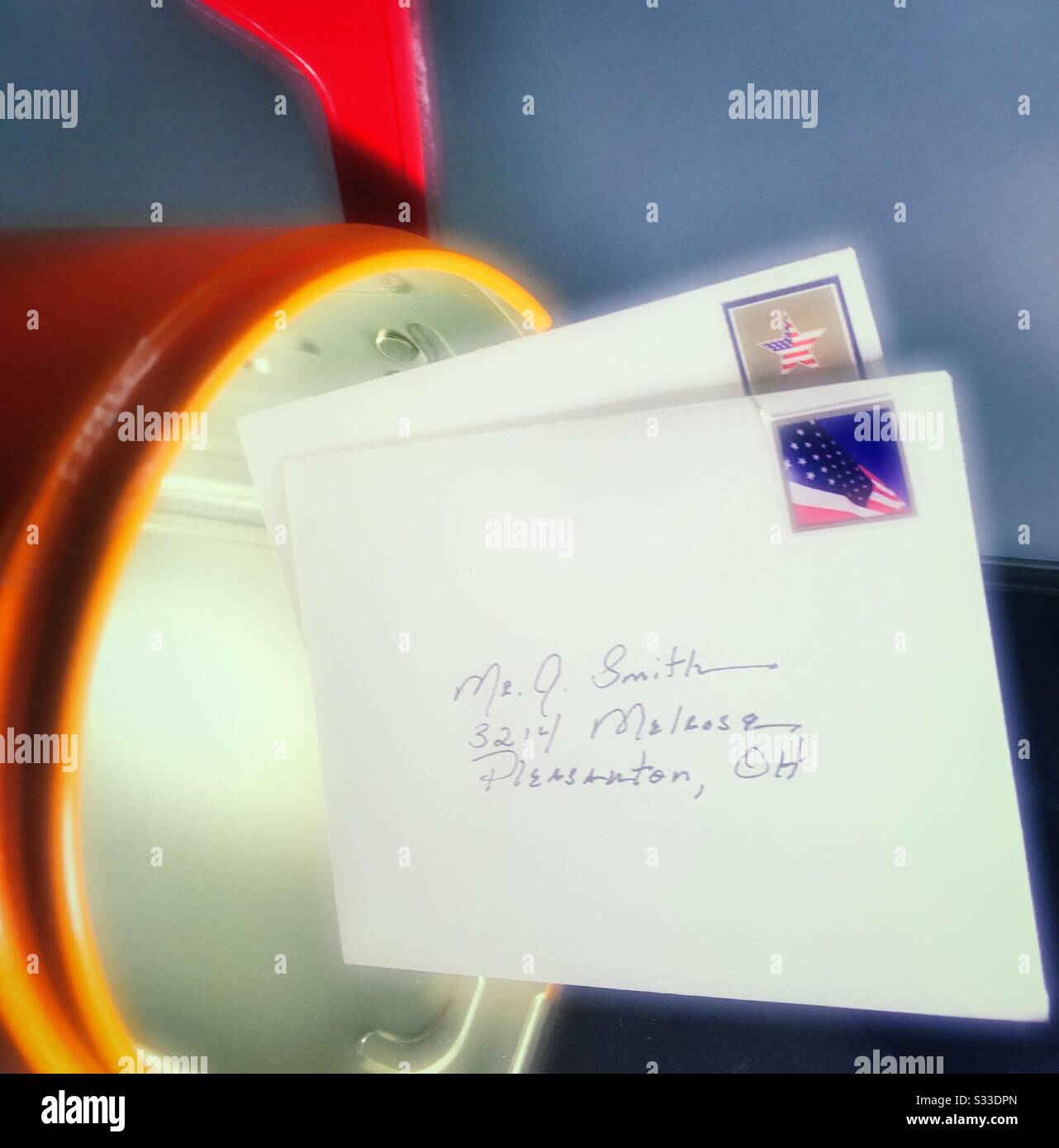 Close up of stamped letters halfway in a bright orange mailbox, USA - Smartphone Captured Stock Image