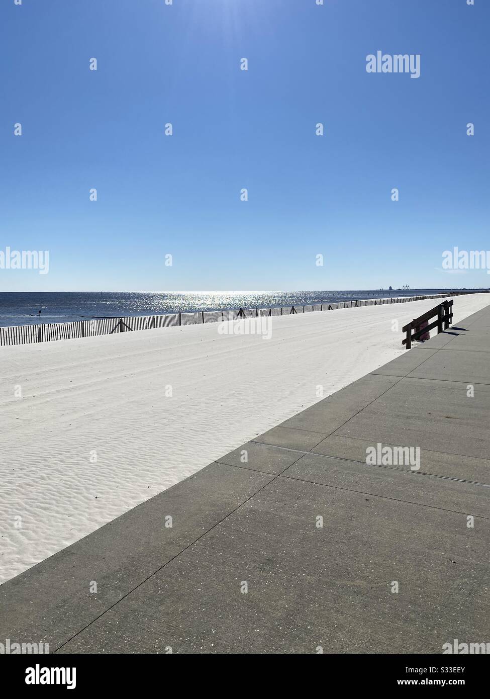 Concrete walkway with steps onto white sand beach with sun reflecting on Gulf of Mexico water, Biloxi, Mississippi - Smartphone Captured Stock Image