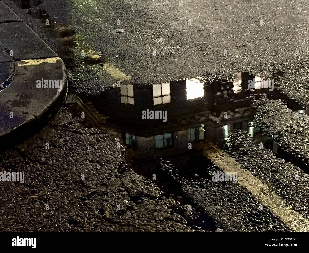 Urban Kerbside reflection in a puddle showing yellow road lines and a building in the reflection - Smartphone Captured Stock Image