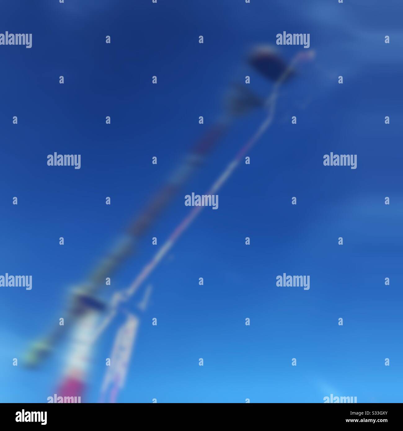 An abstract blurred view of a tall fairground ride swinging agains a clear blue sky. Colourful motion blur with copy space - Smartphone Captured Stock Image