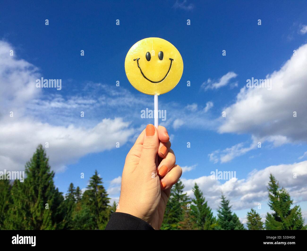 Hand holding smiley face candy against the sky Stock Photo