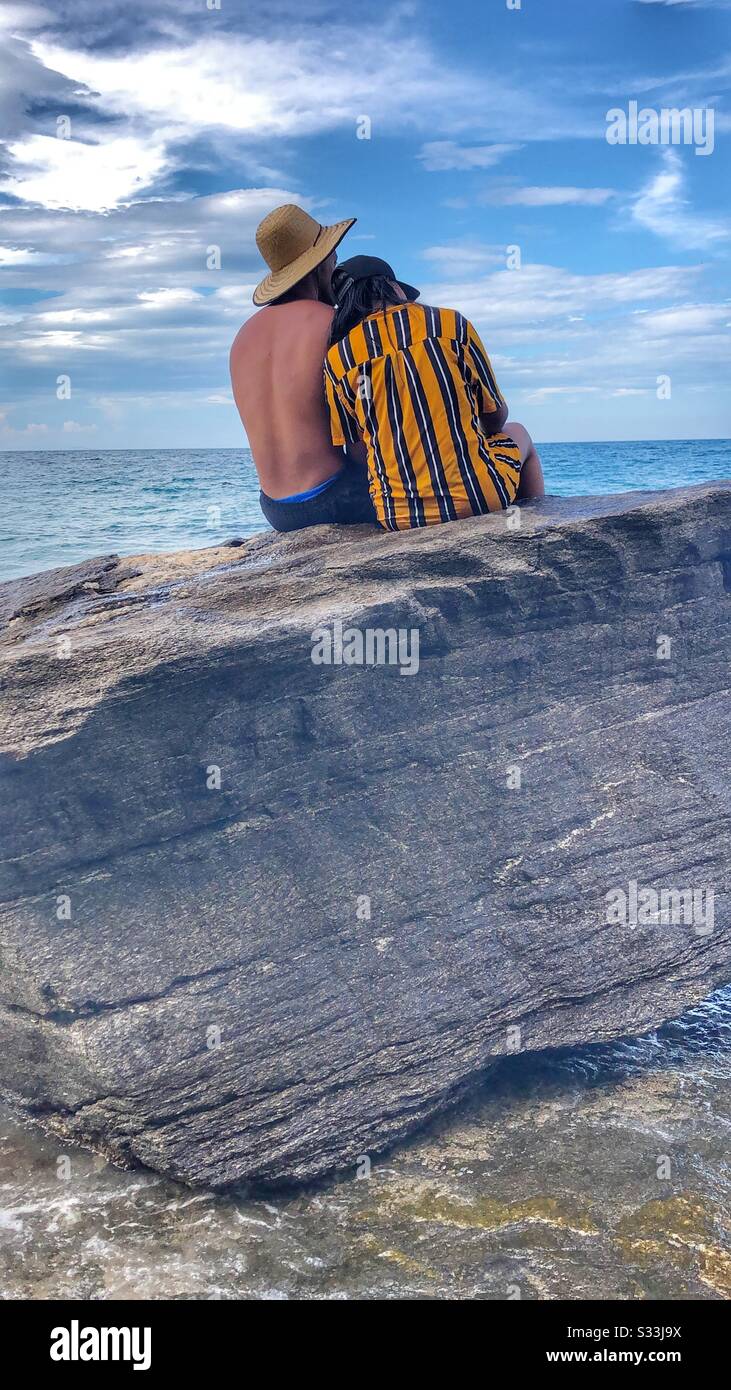 A couple sitting on the rocks enjoying the seaside together. - Smartphone Captured Stock Image