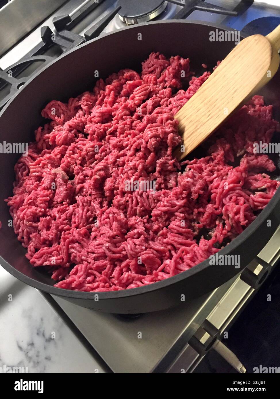 Raw ground beef being browned in a large skillet and stirred with the wooden spatula - Smartphone Captured Stock Image