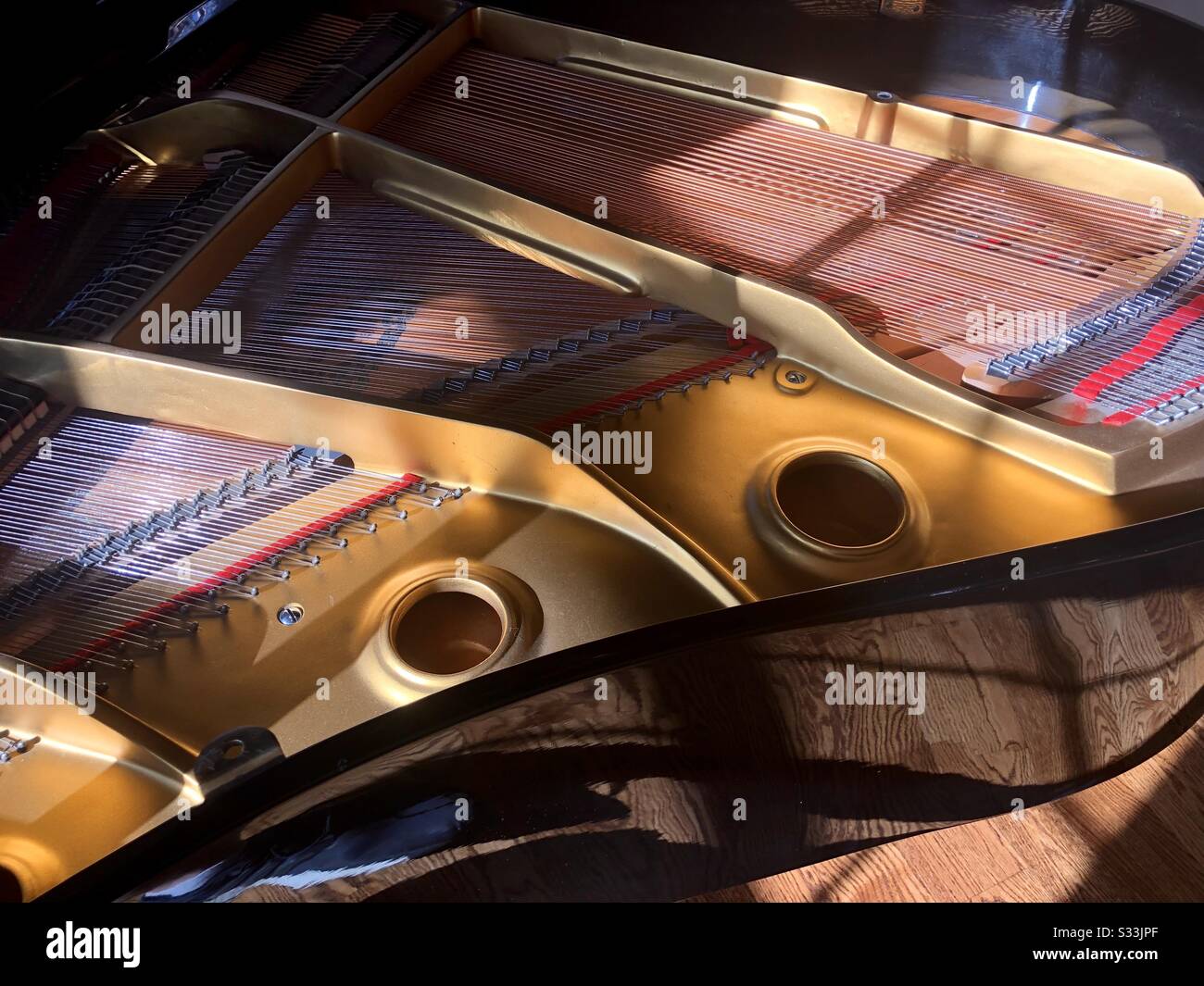 View from above of the inside of a baby grand piano, including soundboard, brass, strings, and pegs Stock Photo