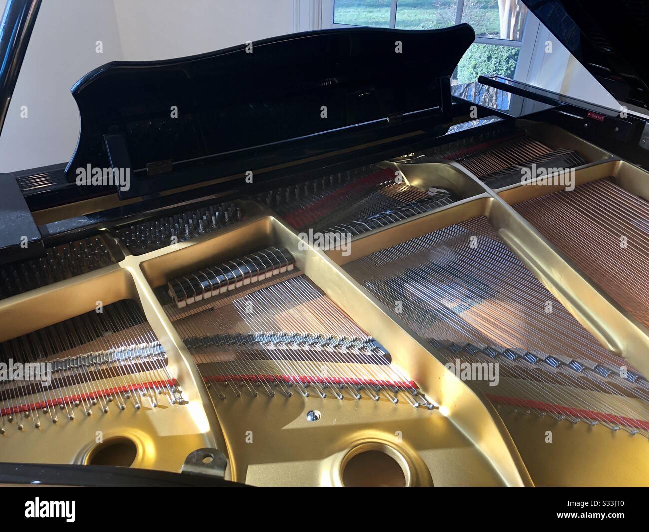 View inside a baby grand piano with the top open.  Picture includes the brass frame, front end of strings, hammers, and music stand. Stock Photo
