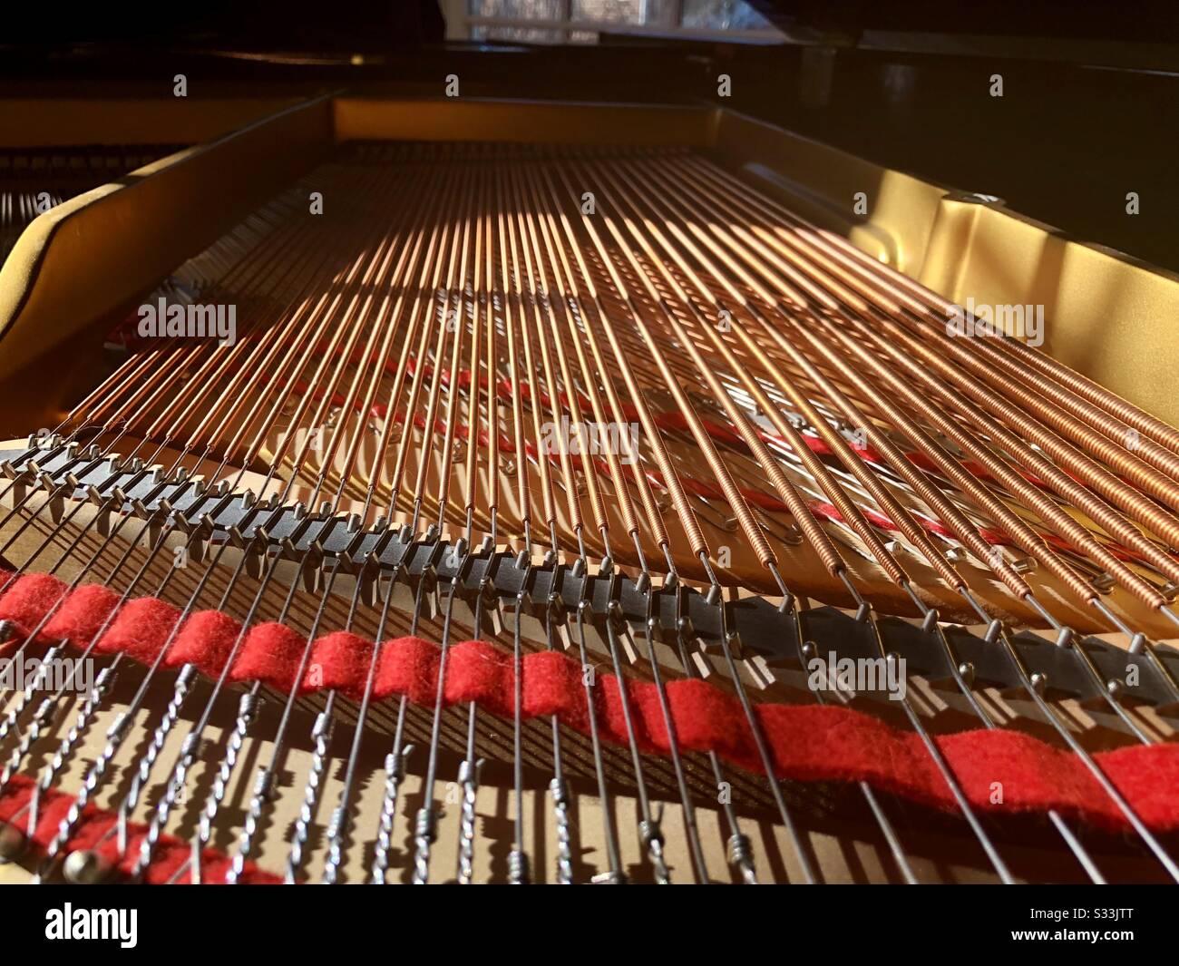 Headlong perspective of the inside of a baby grand piano.  Strings, felt, brass structure, and knots are visible. Stock Photo