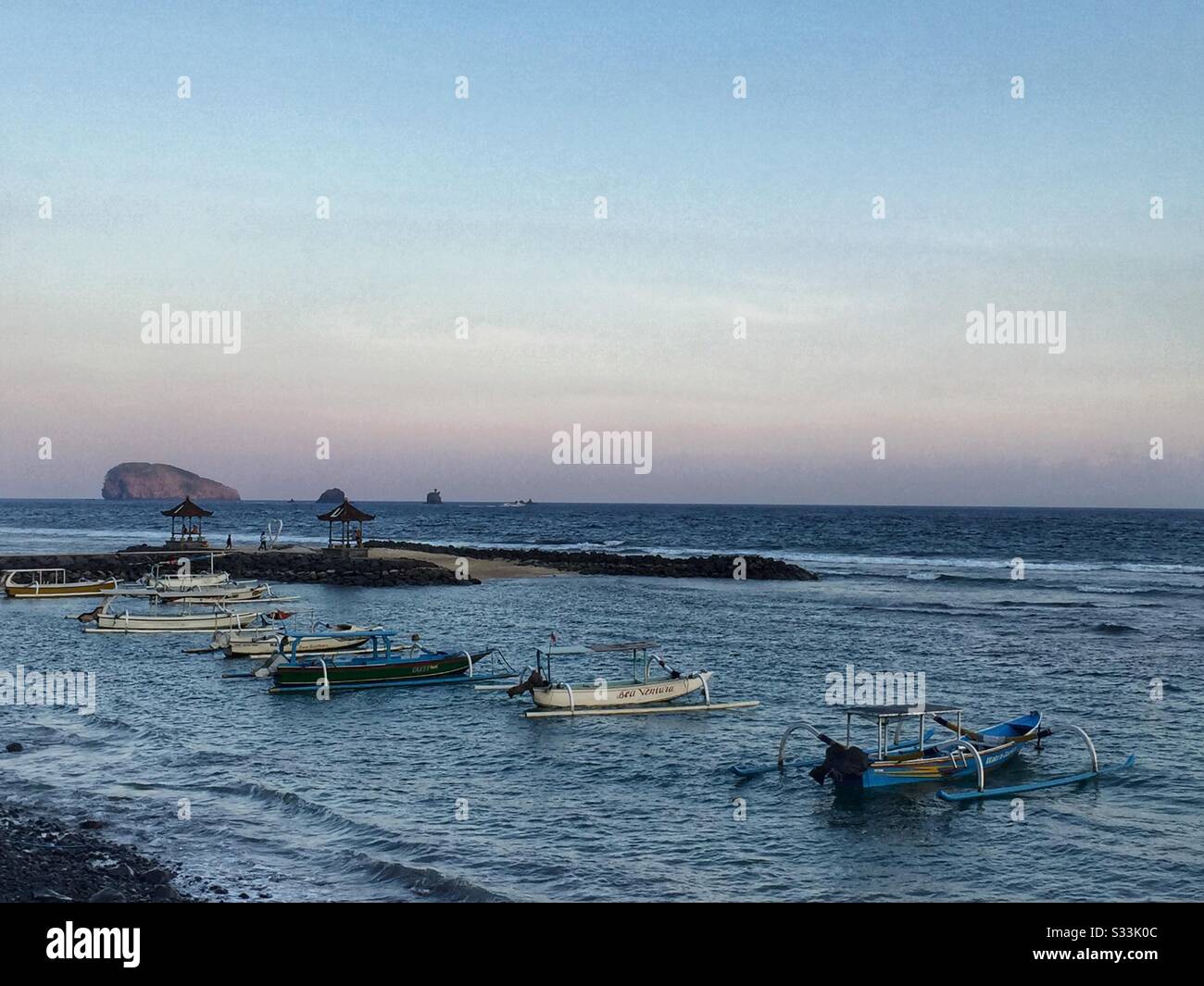 Traditional outrigger fishing boats moored off the beach at sunset, Candidasa, Bali, Indonesia - Smartphone Captured Stock Image