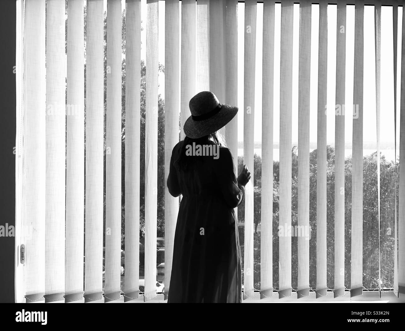 Black and white photo of a woman near the blinds Stock Photo