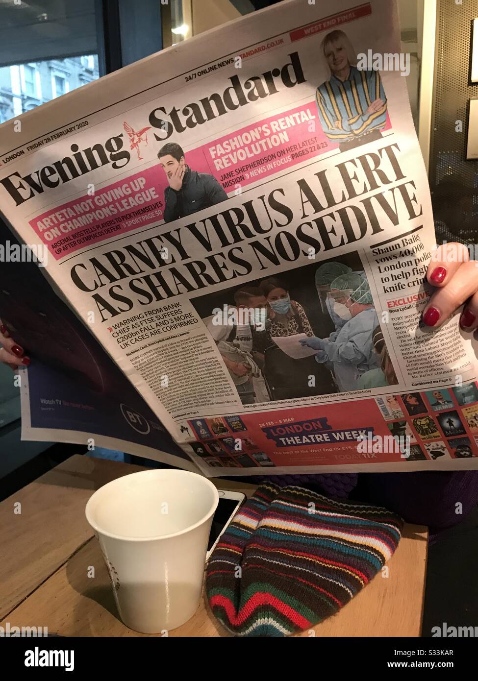 London, England, UK 28th February 2020. Coffee shop customer in London reads Evening newspaper headlines of Coronavirus. - Smartphone Captured Stock Image