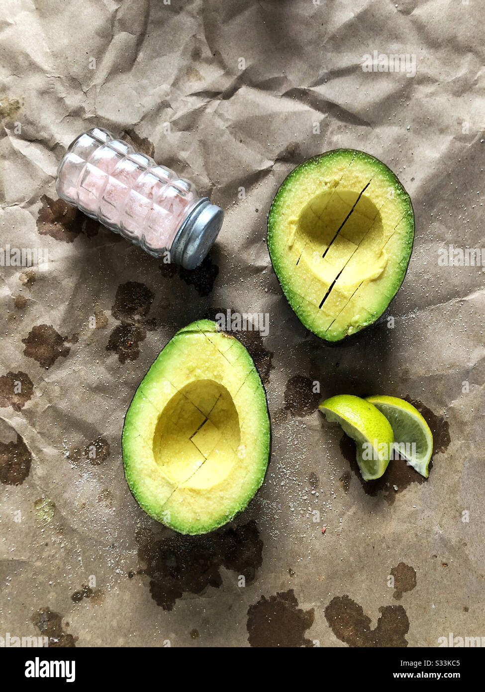 Avocado cut into halves and scored with a knife, served with pink Himalayan sea salt and slices of key limes as a healthy snack on the go - Smartphone Captured Stock Image