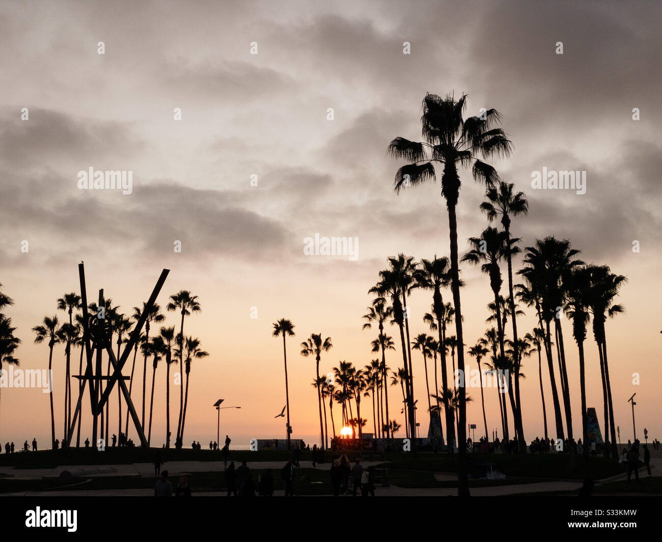 VENICE BEACH, CA, JAN 2020: silhouetted people and palm trees near the beach with orange sky at sunset - Smartphone Captured Stock Image