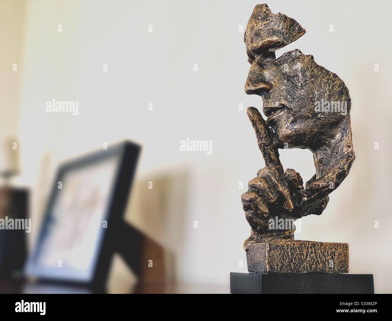 A close up and selective focus shot of an abstract face holding index finger to mouth, indicating silence, quiet, shh, shhh, sh. Modern home decor ornament - Smartphone Captured Stock Image