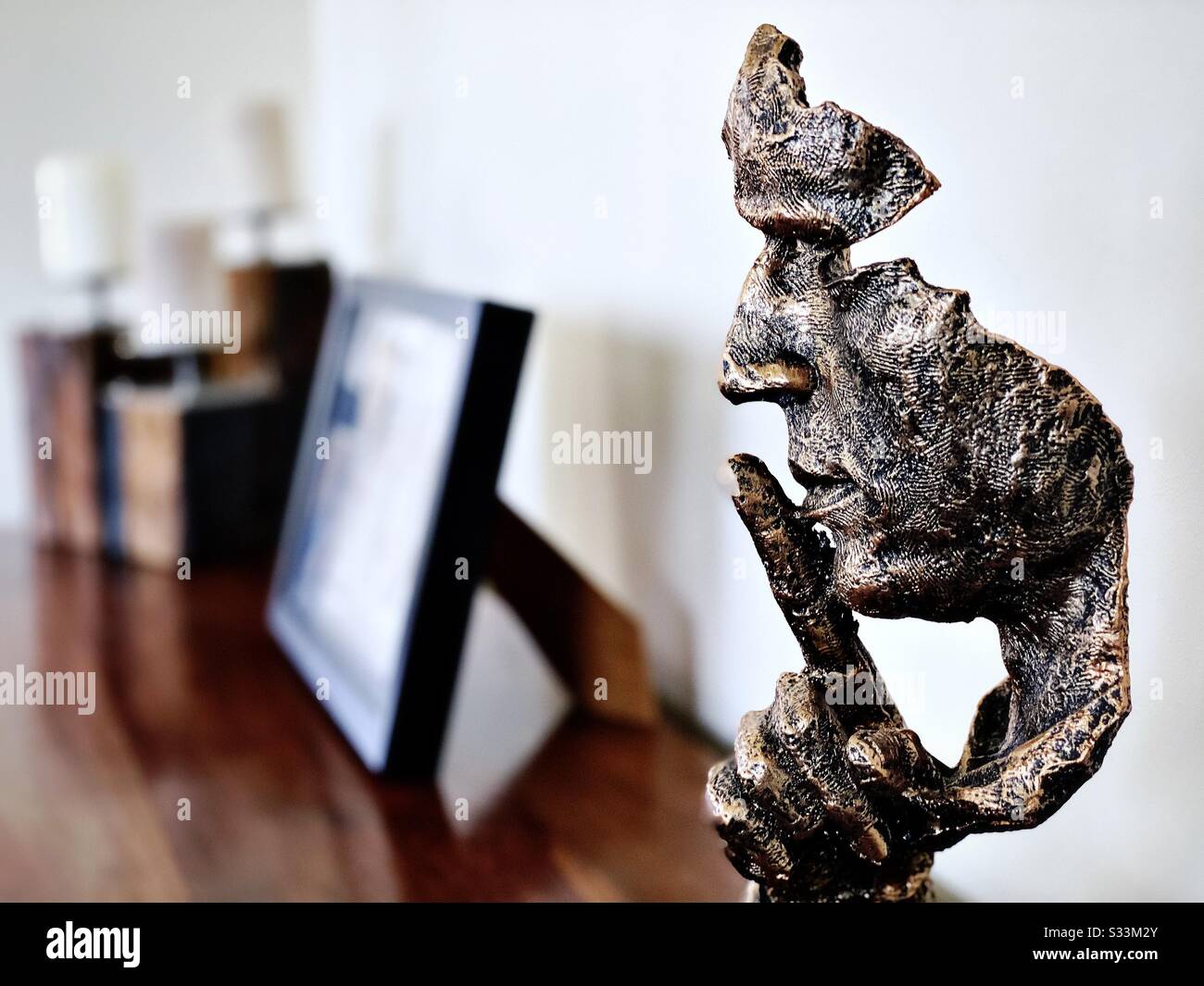 A close up high contrast shot of a modern head statue on a home sideboard with blurry picture frame in background. Finger gesture for peace and quiet. Finger raised to mouth. Shh - Smartphone Captured Stock Image