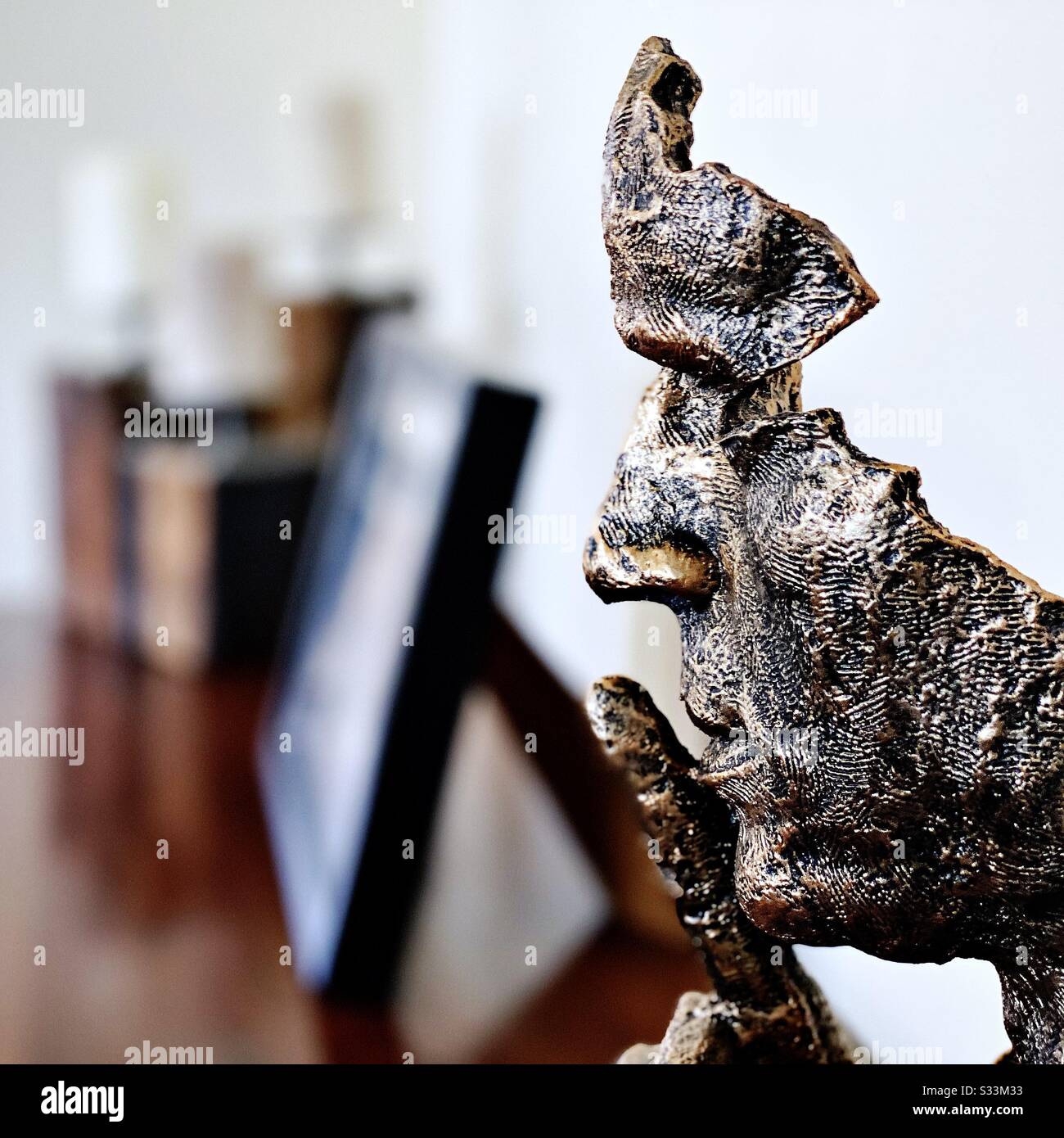 A close up high contrast shot of a modern head statue on a home sideboard with blurry picture frame in background. Finger gesture for peace and quiet. Finger raised to mouth. Shh - Smartphone Captured Stock Image