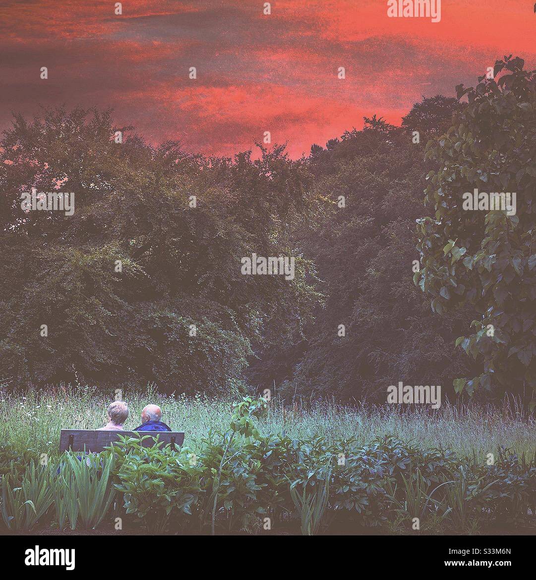 Old and elderly couple, man and wife sat outside beneath an eerie blood red sky.  Spooky sky.  Menacing sky.  Uncertain future looms - Smartphone Captured Stock Image Old and elderly couple, man and wife sat outside beneath an eerie blood red sky.  Spooky sky.  Menacing sky.  Uncertain future looms - Smartphone Captured Stock Image