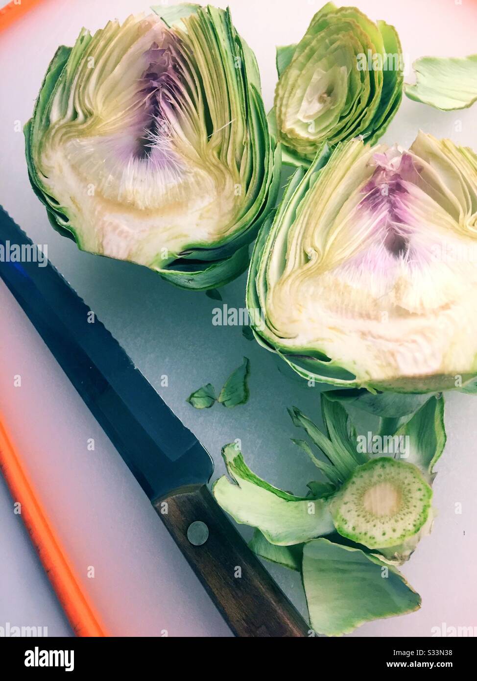 Whole raw artichoke sliced in two on a cutting board with a chefs knife - Smartphone Captured Stock Image